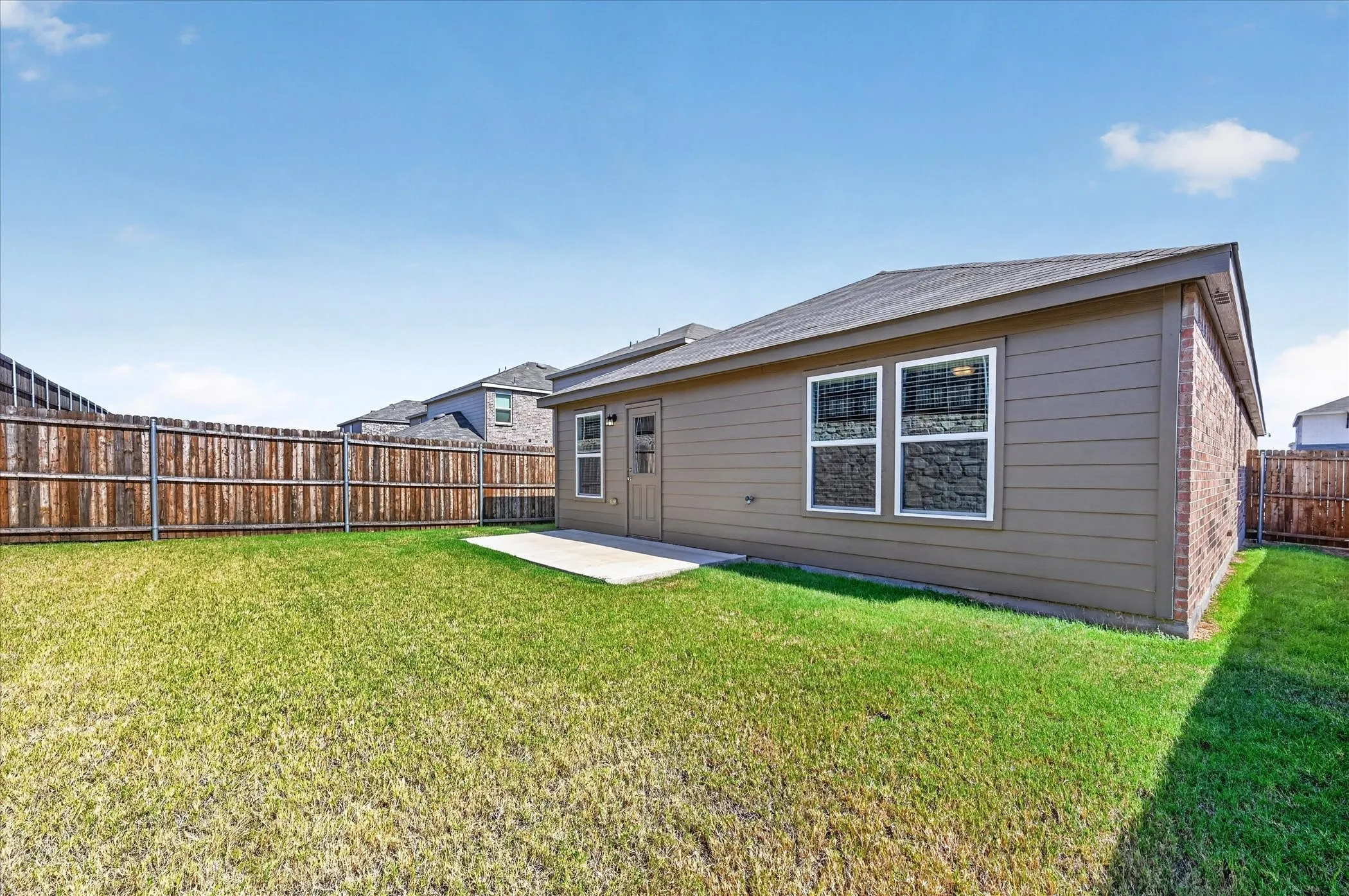 Expansive backyard featuring a manicured lawn, full privacy fencing, and a concrete patio
