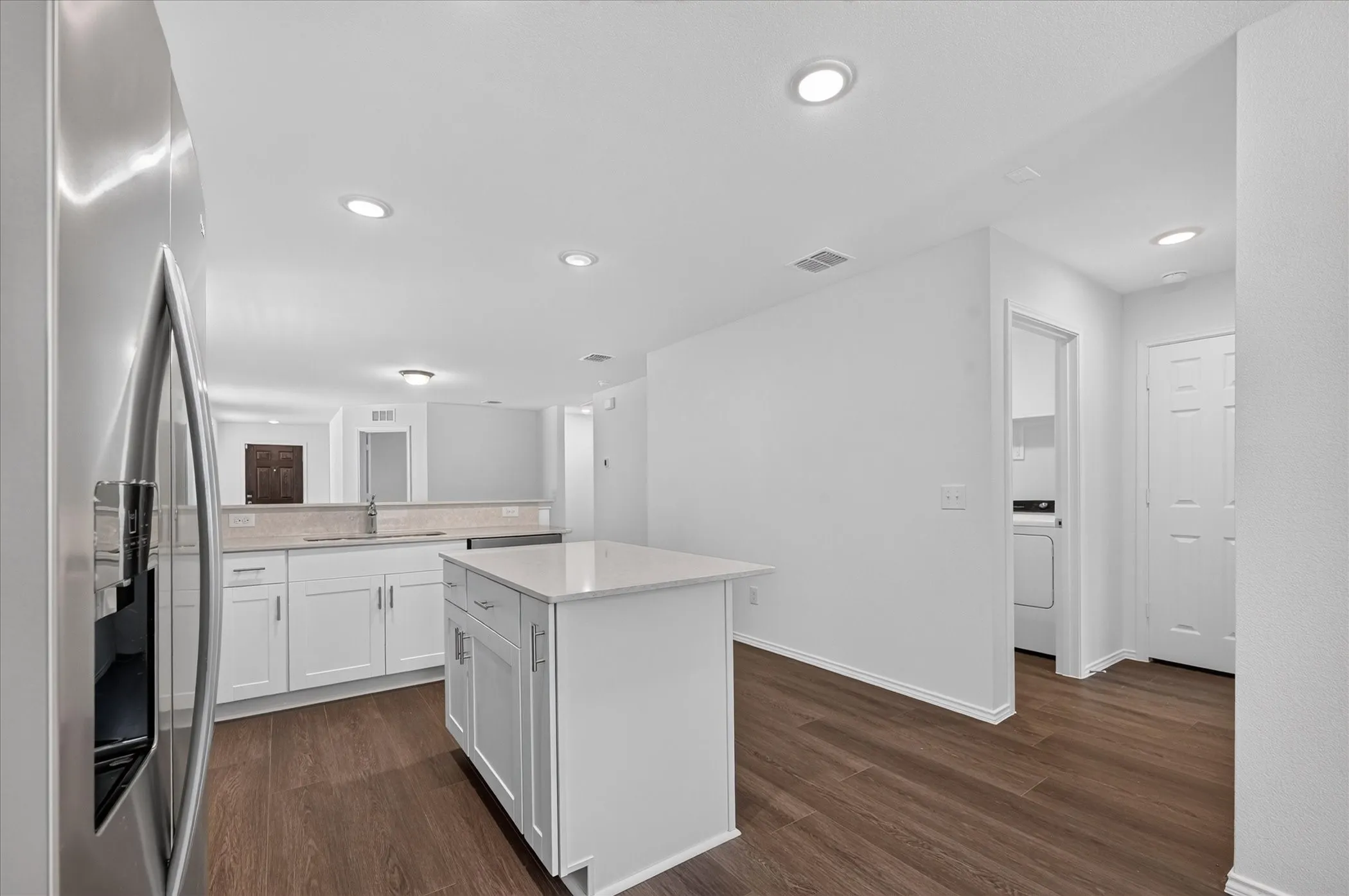 Kitchen featuring a central island with a light-toned countertop, wood-finish flooring, white cabinetry, and stainless steel appliances