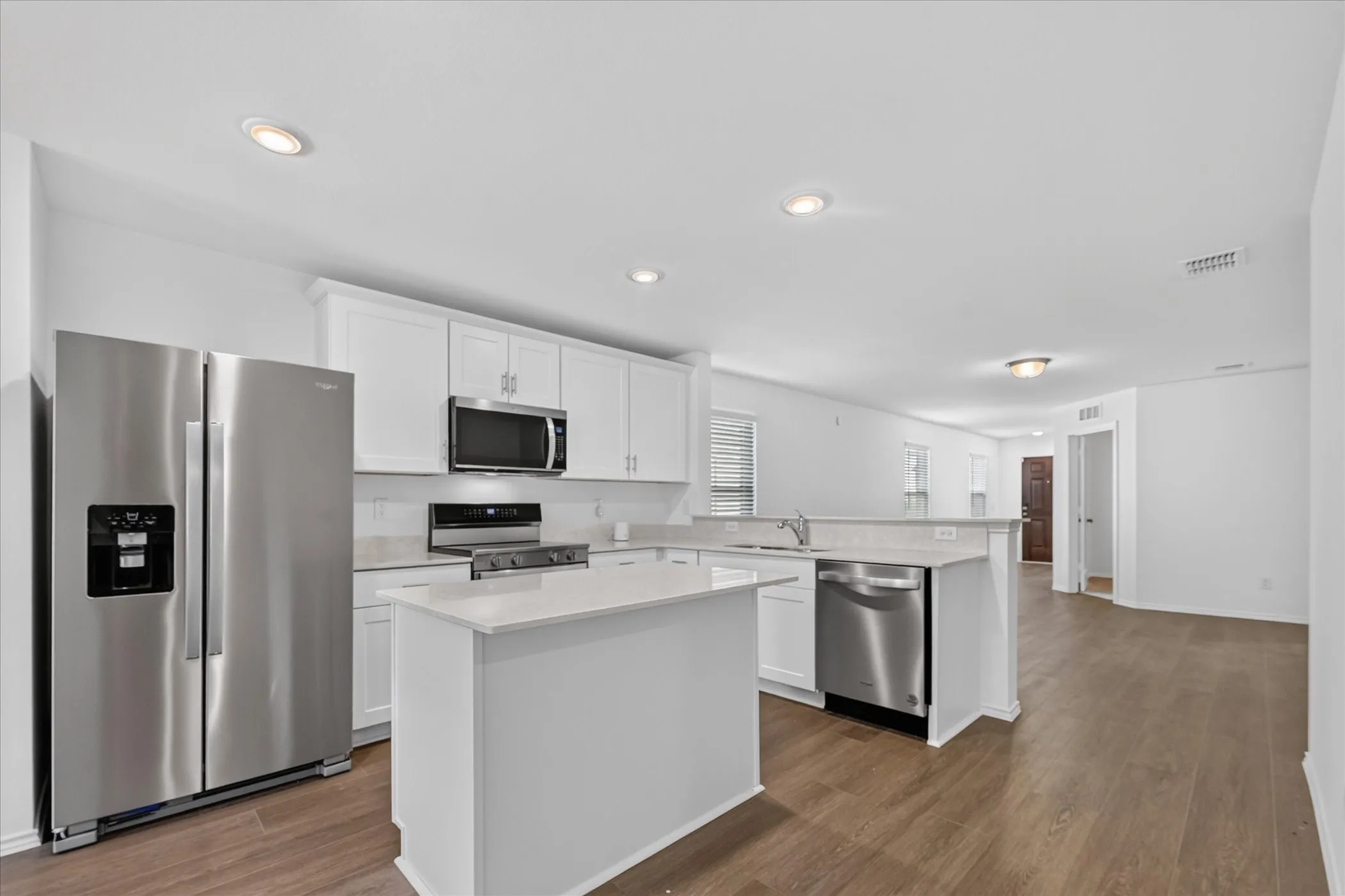 Kitchen featuring a central island, stainless steel appliances, white cabinetry, light-toned countertops, and wood-finish flooring