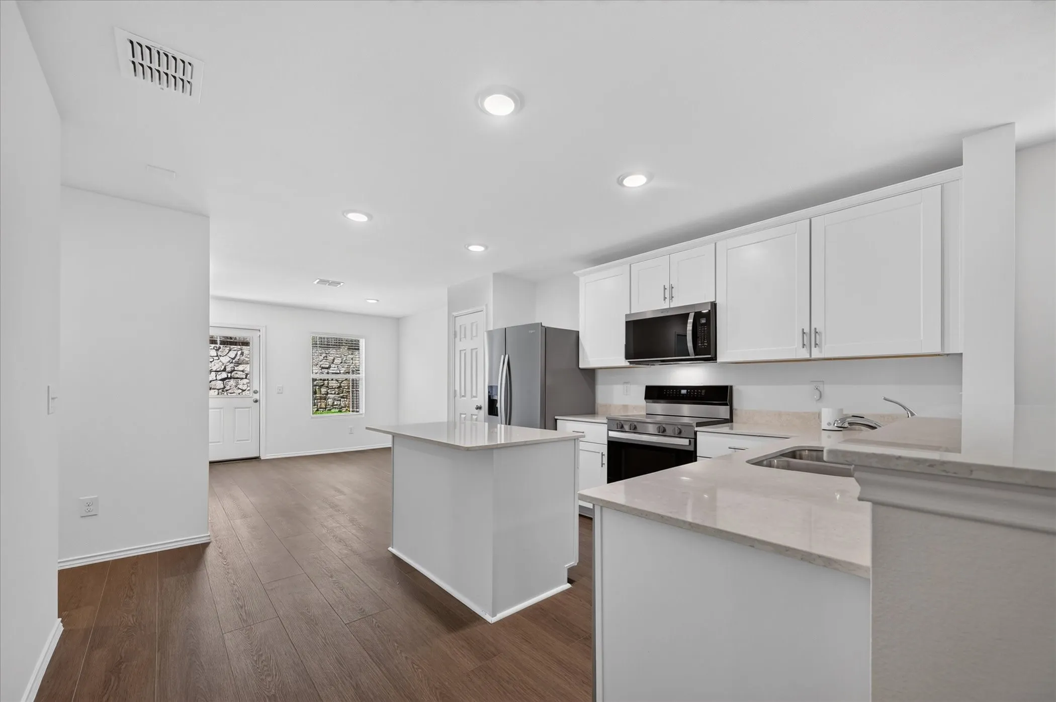 Kitchen with white cabinetry, light-toned countertops, stainless steel appliances, and dark wood-finish flooring
