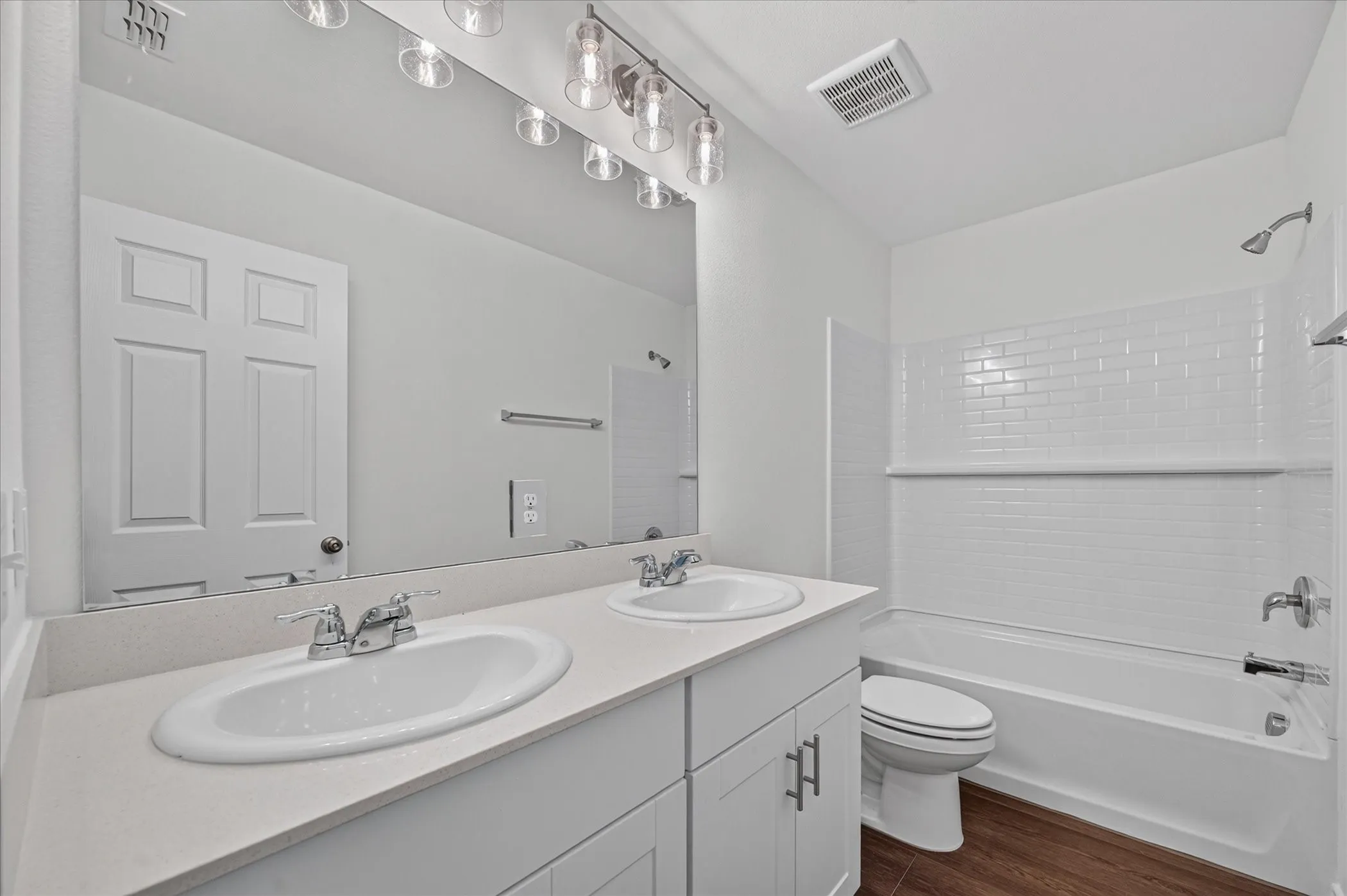 Bathroom featuring a dual-sink vanity with light-toned countertops, a full-width mirror, and overhead vanity lighting