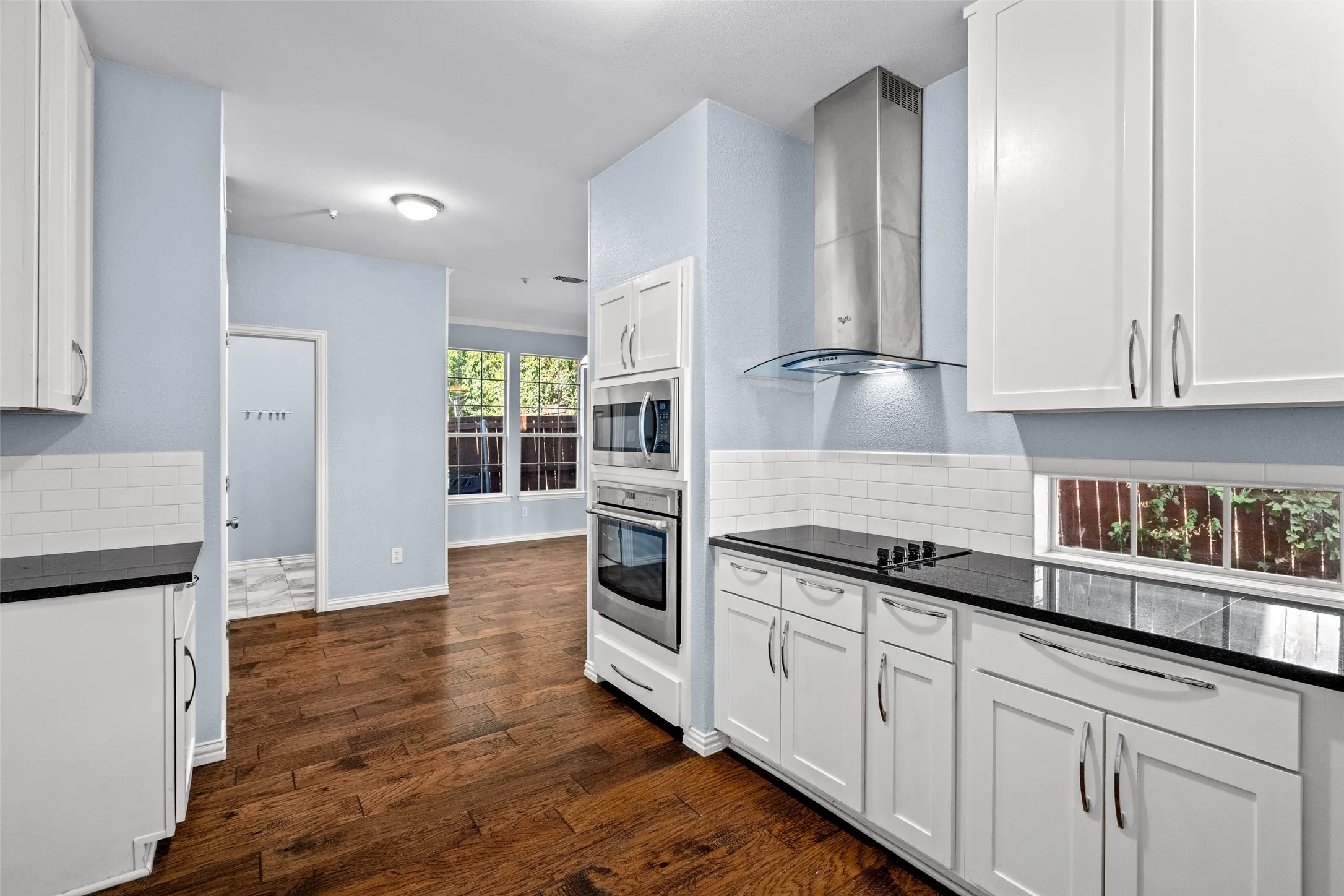 Kitchen with wood-finish flooring, white cabinetry, integrated stainless steel appliances, dark countertops, and white subway tile backsplash