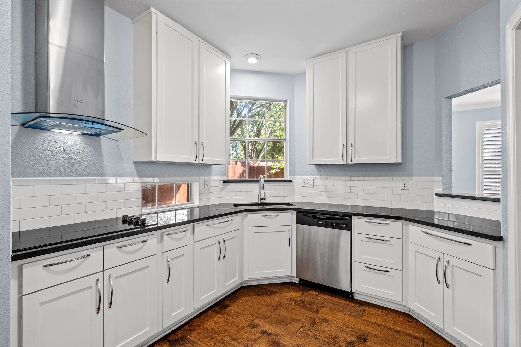 White cabinetry, dark countertops, a stainless steel dishwasher, and wood-finish flooring