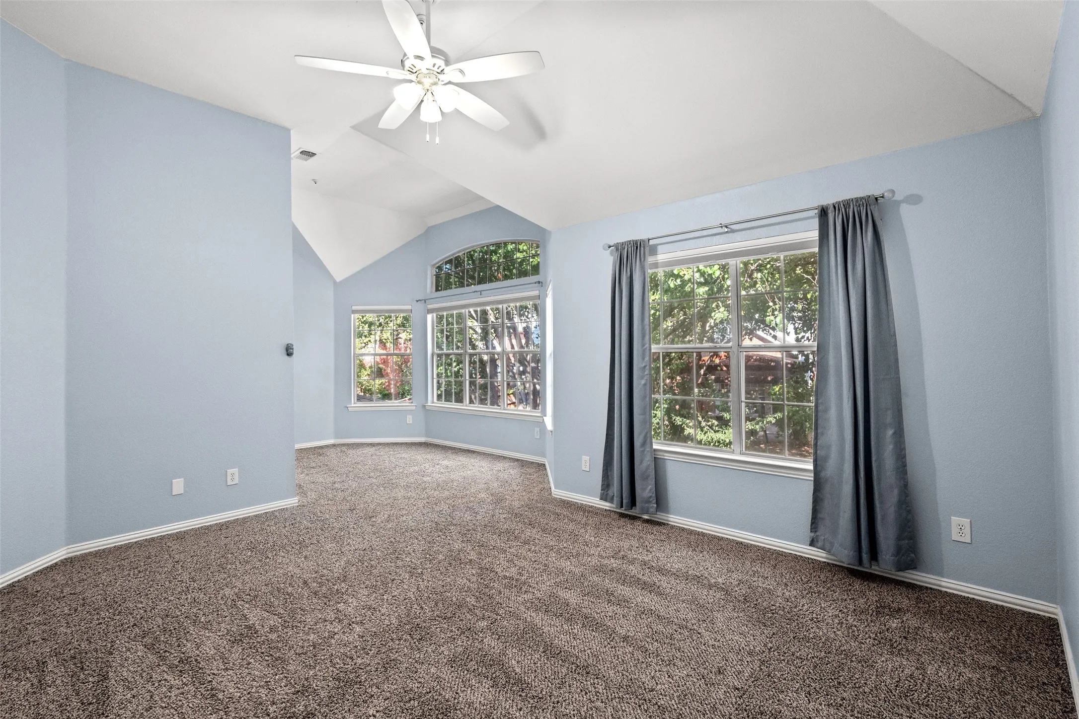 Vaulted ceilings, a ceiling fan, and multiple windows with an arched transom window
