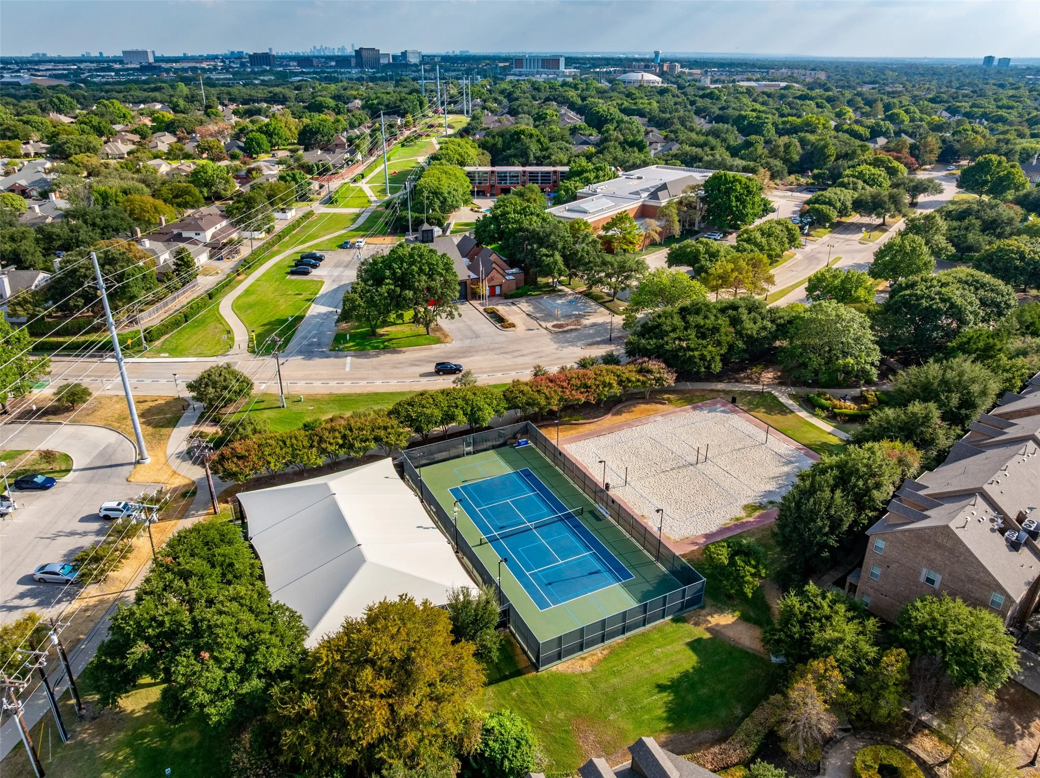 Aerial perspective showcasing a tennis court, sand volleyball court, and adjacent covered structure