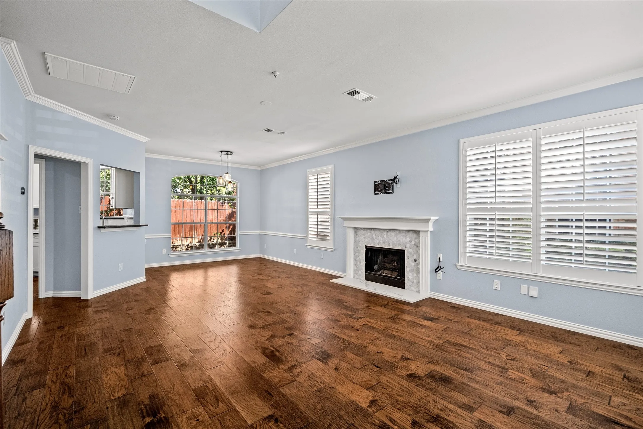 Hardwood flooring, fireplace with tile surround, white plantation shutters, crown molding, and recessed lighting