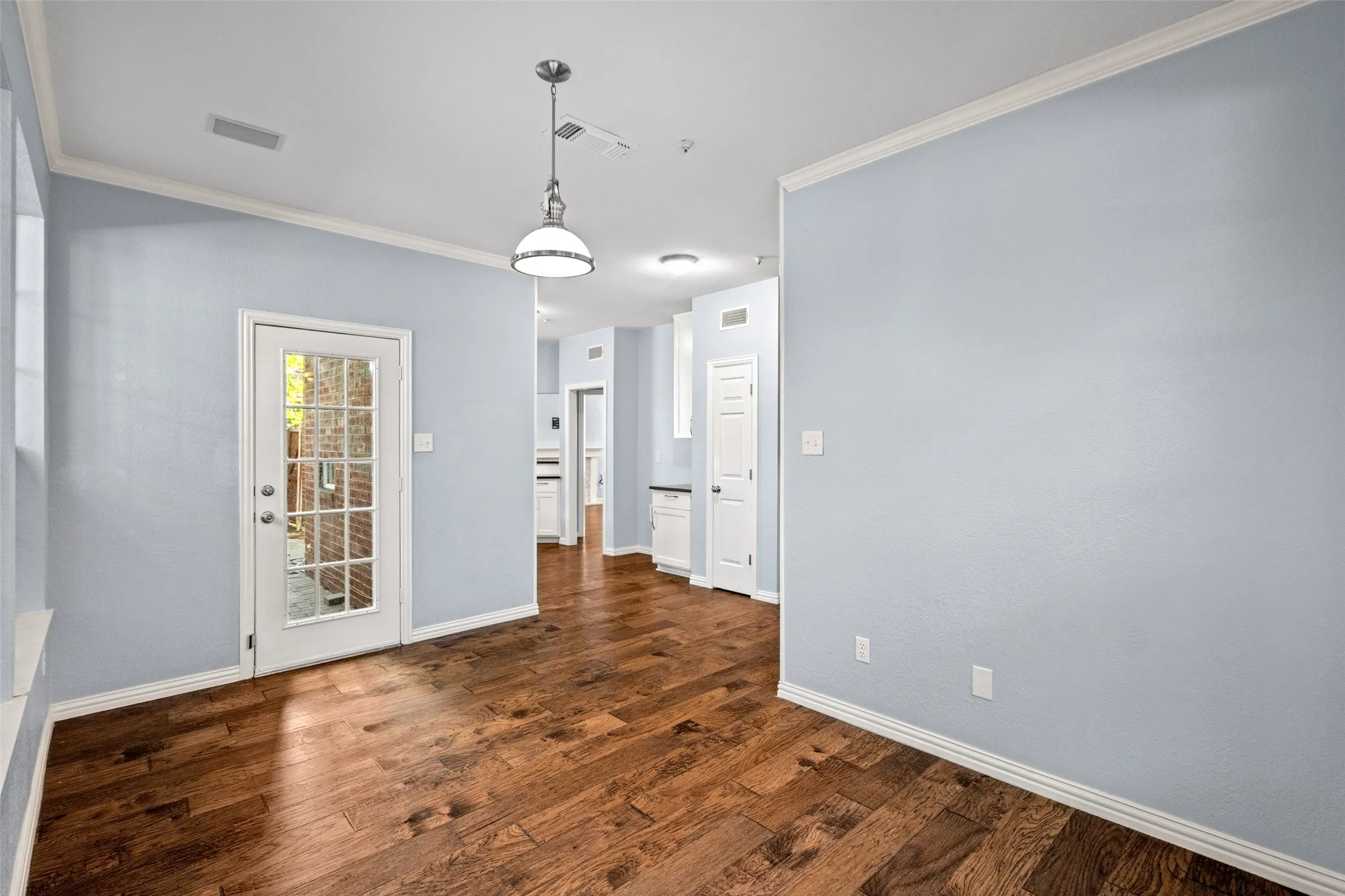 Wood-finish flooring throughout, white crown molding, and a paneled glass door