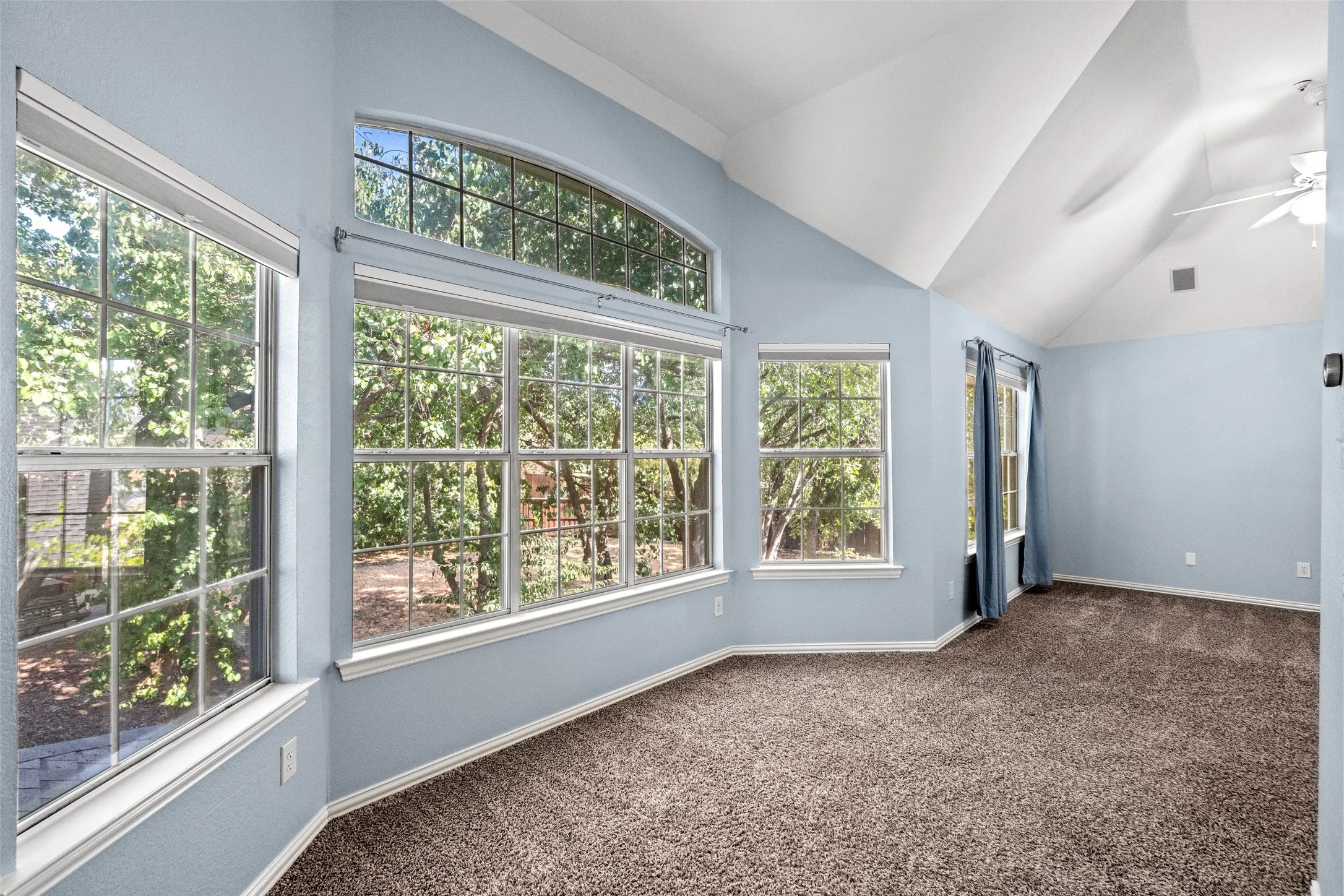 Vaulted ceiling with a ceiling fan, multiple windows with grid patterns, an arched transom window, and textured wall finish