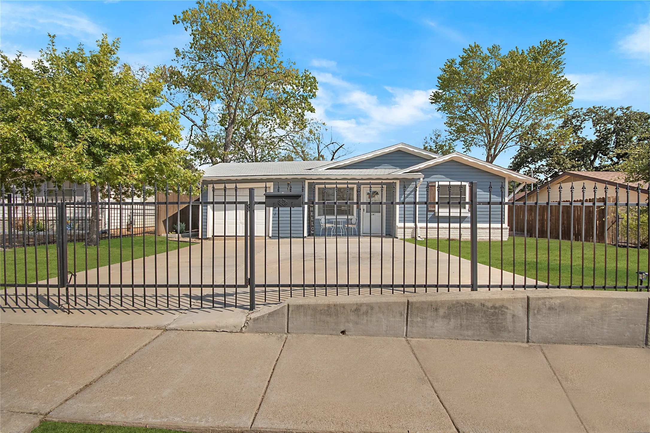 Blue siding exterior with white trim, a fenced front yard, mature trees, and a concrete driveway