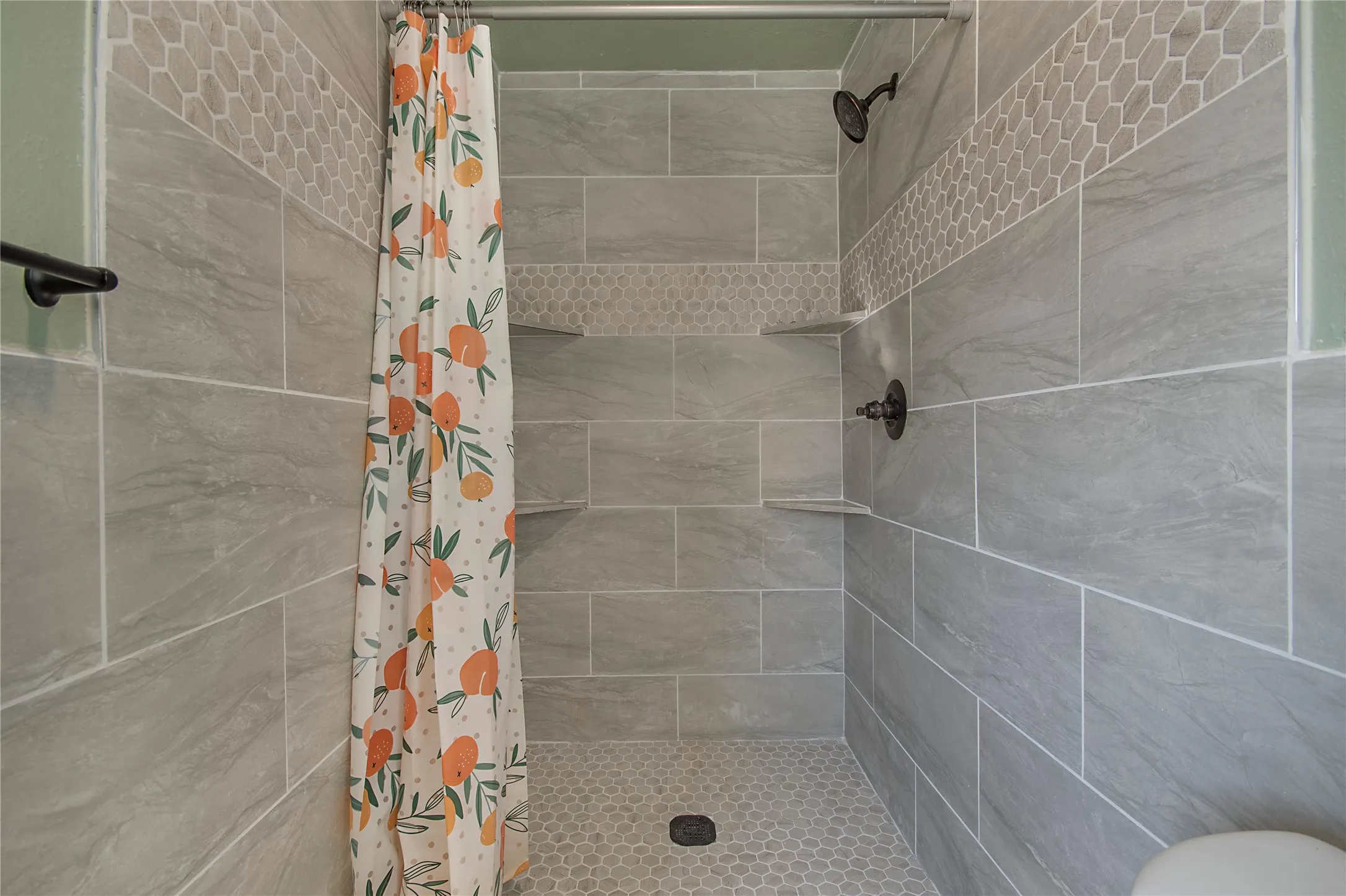 Shower enclosure with light grey tile walls, a decorative honeycomb tile band, and built-in corner shelving