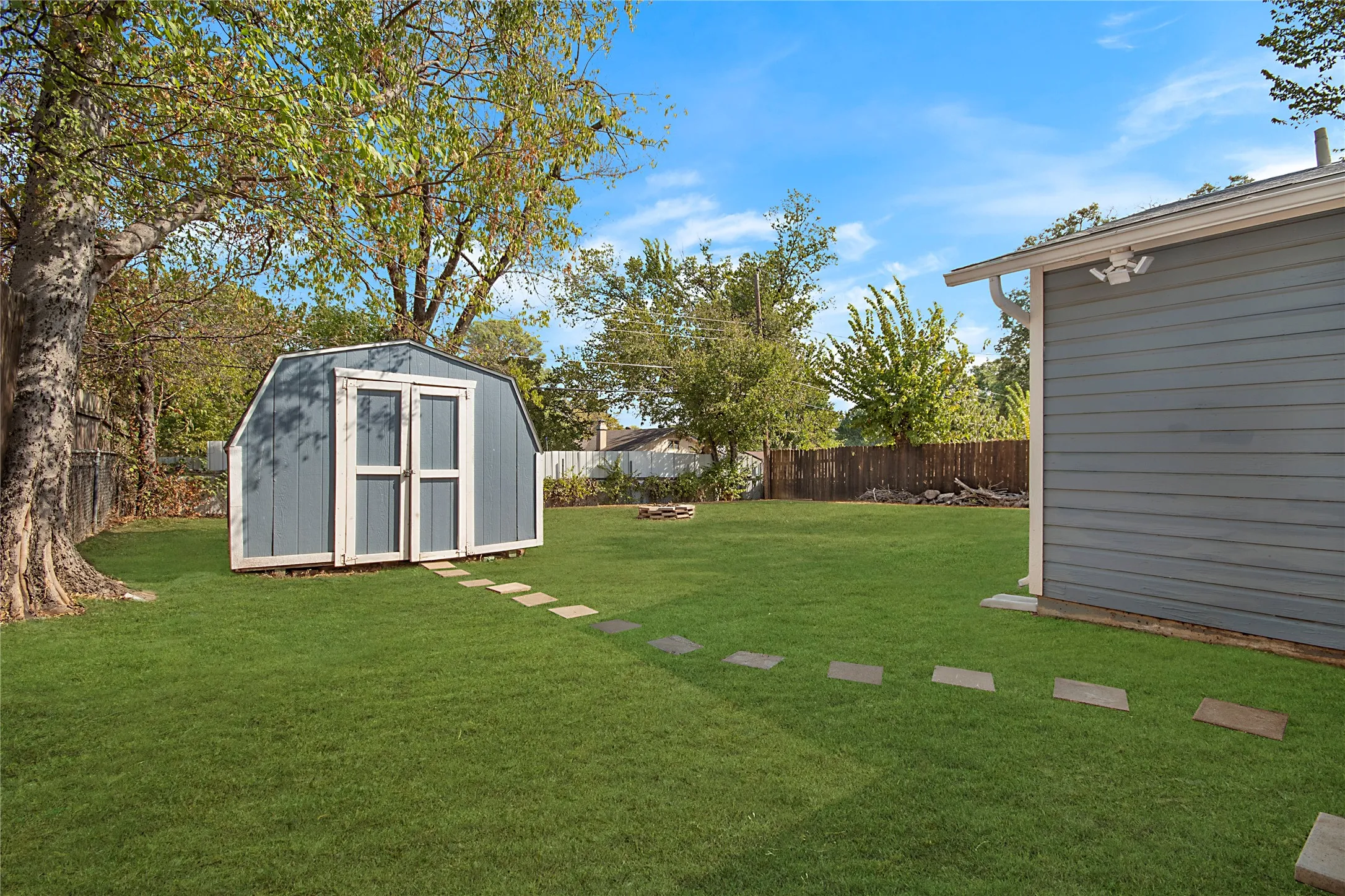 Expansive green lawn featuring a detached shed with double barn doors, stepping stone path, and wood fence surround
