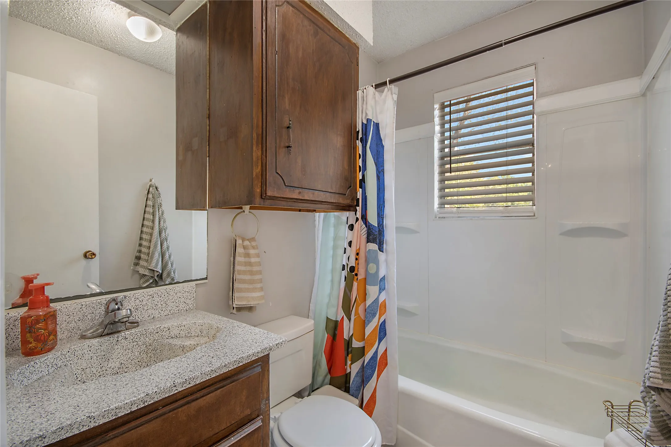 White bathtub with an integrated shower surround and a window with blinds