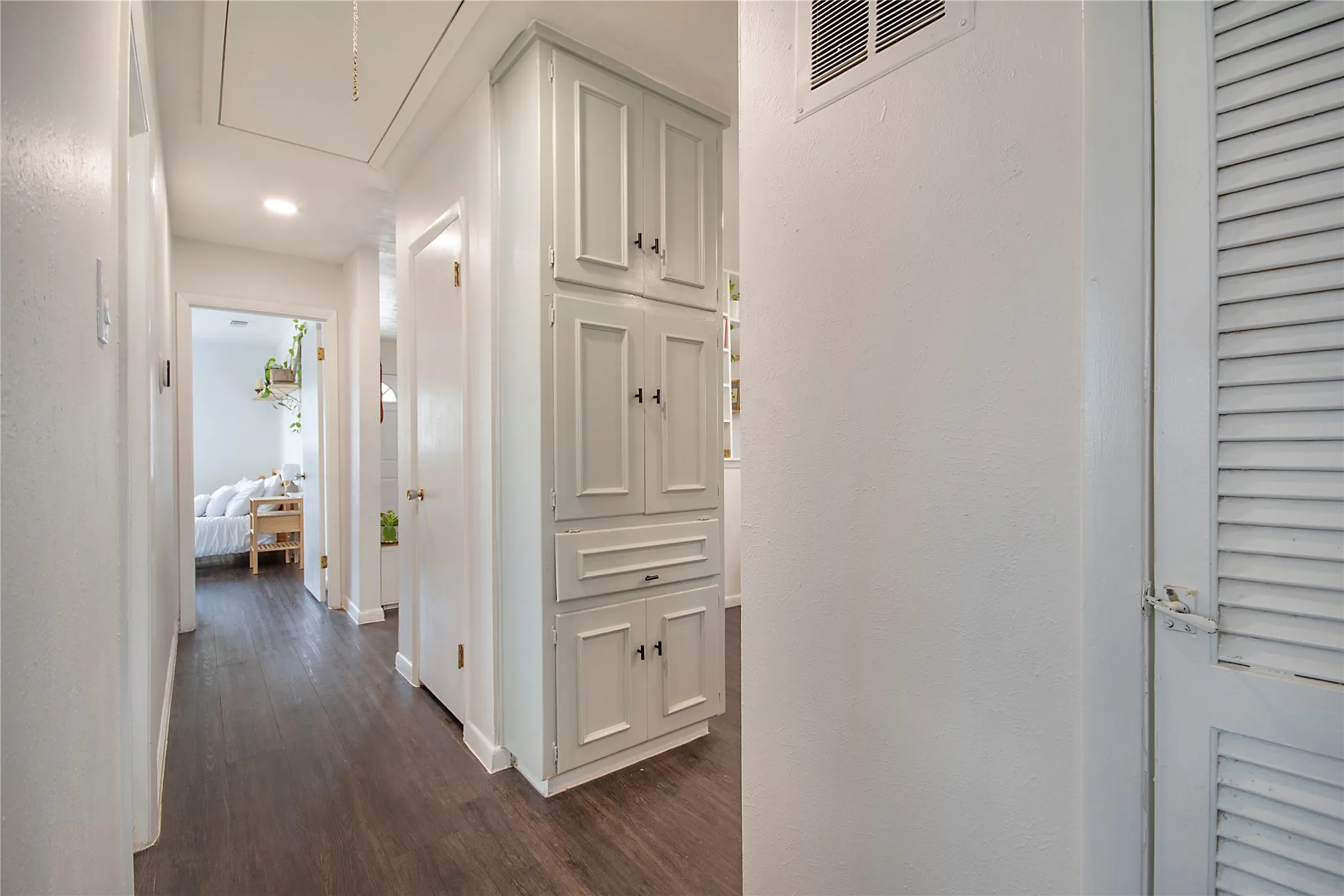 Hallway featuring wood-finish flooring, built-in cabinetry with paneled doors, recessed lighting, and a louvered door