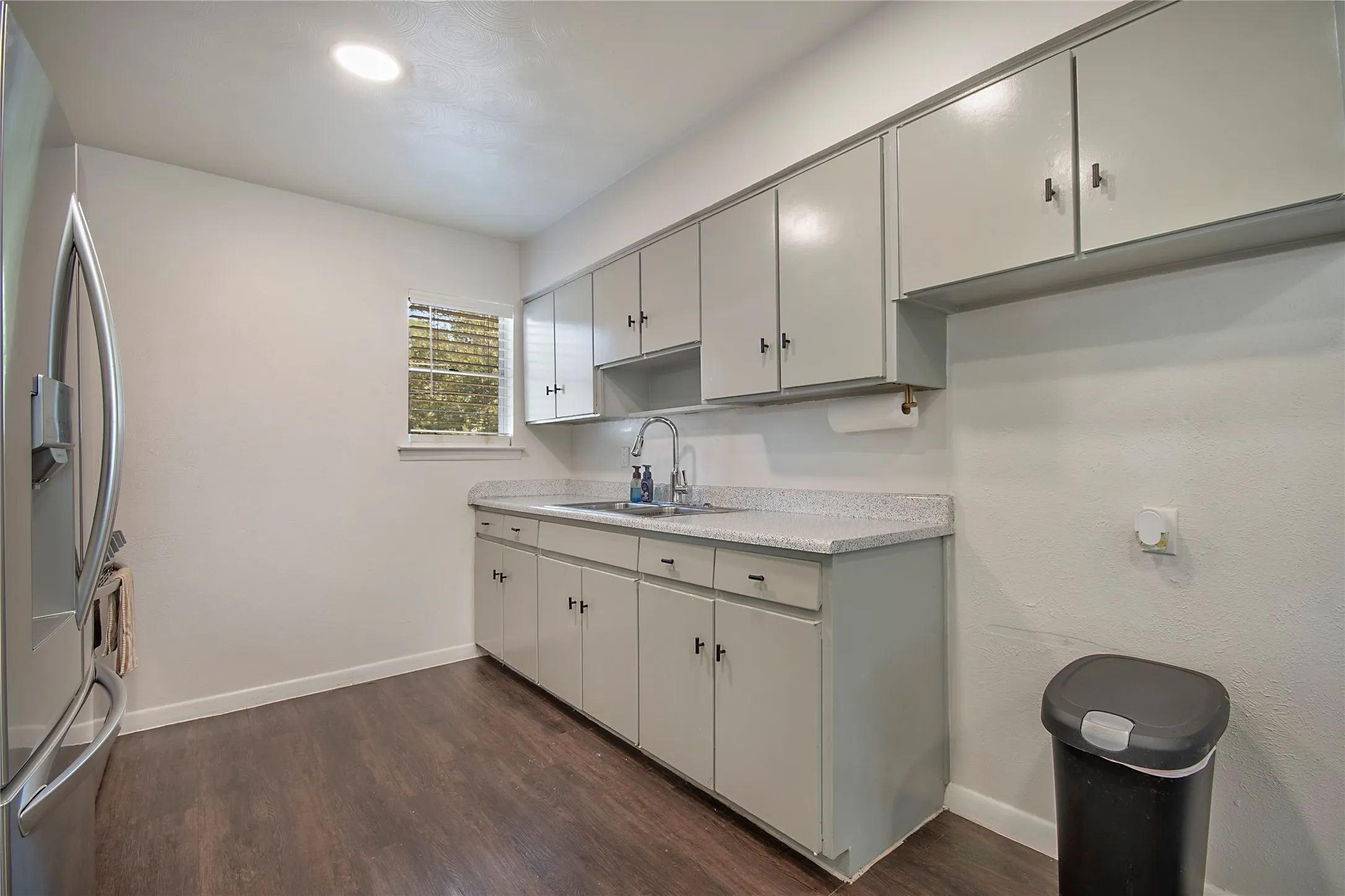 Galley kitchen with white cabinetry, light countertops, stainless steel sink, and wood-finish flooring