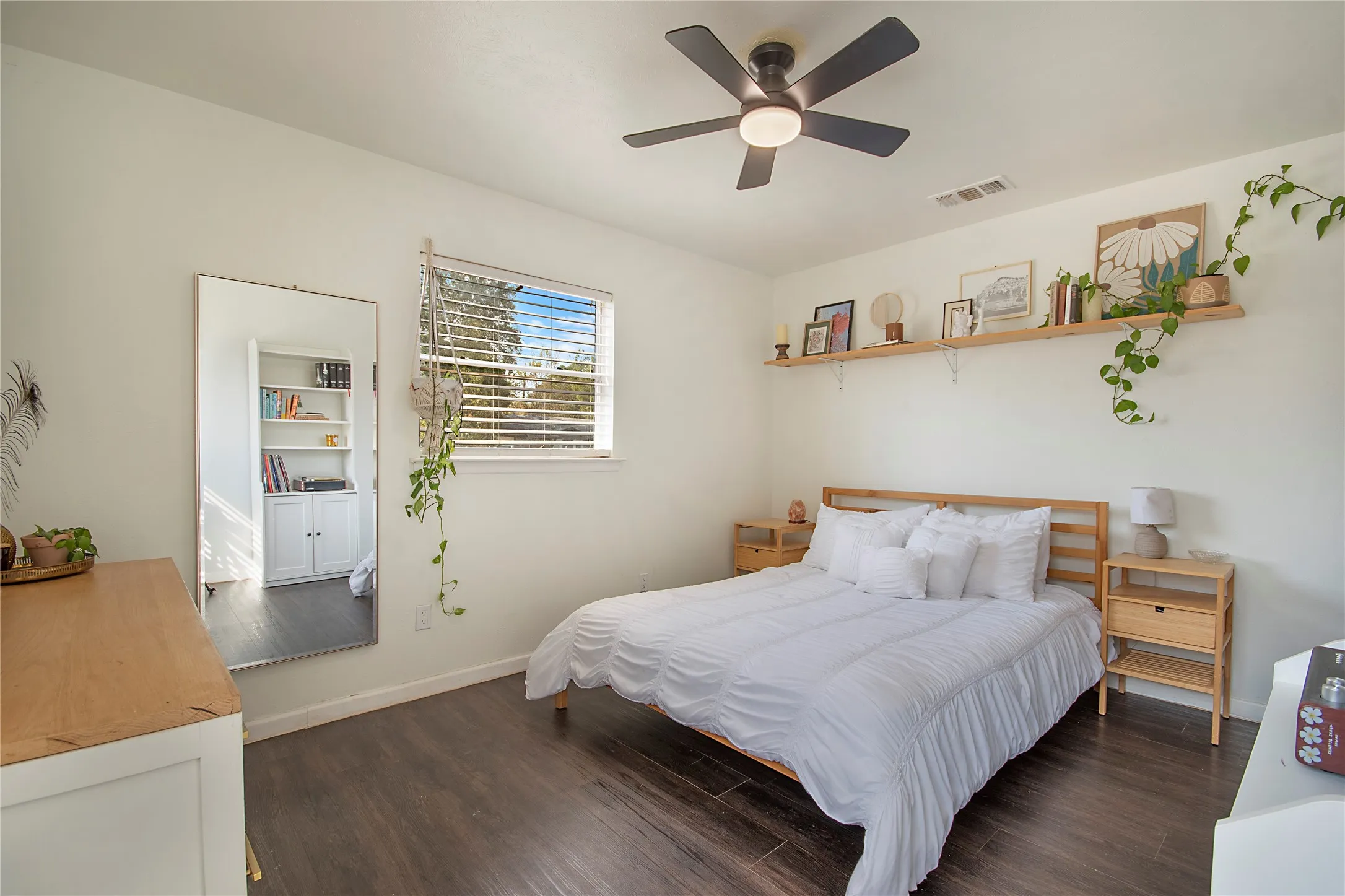 Wood-finish flooring, white walls, a ceiling fan with integrated lighting, and a window with blinds