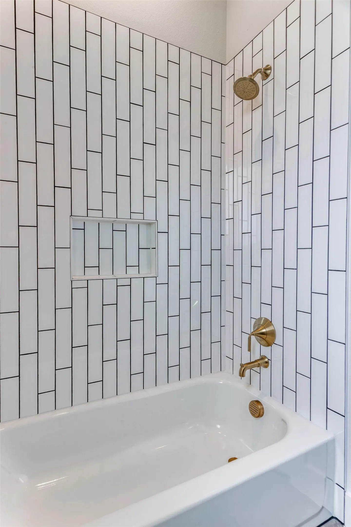 White subway tile surround with dark grout, integrated shower niche, and brass fixtures