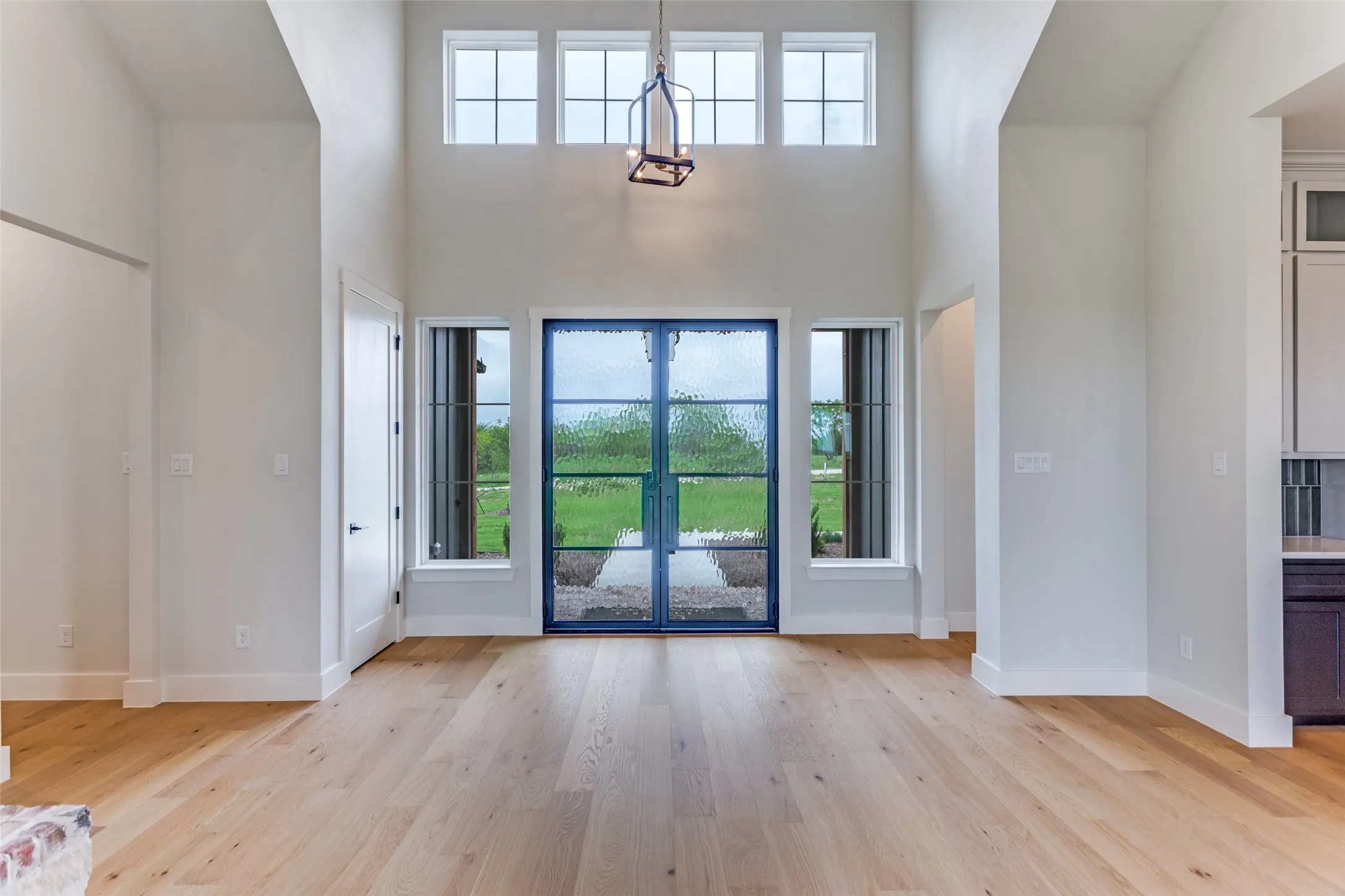 Soaring ceilings with transom windows, wood-finish flooring, and a contemporary entryway featuring a double door with textured glass