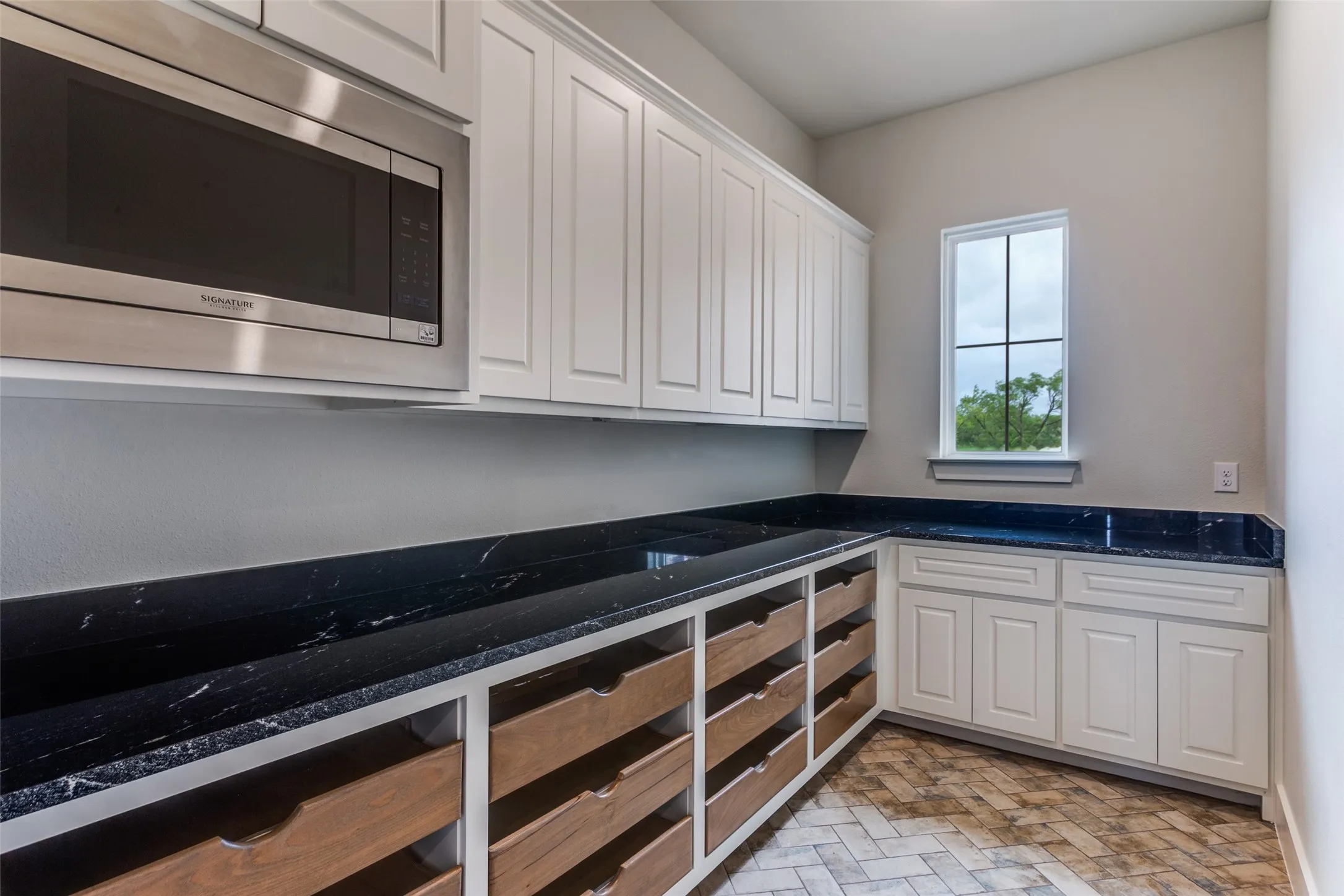 Built-in stainless steel microwave, extensive white cabinetry, dark stone countertops, wood-finish drawers, and herringbone-patterned flooring