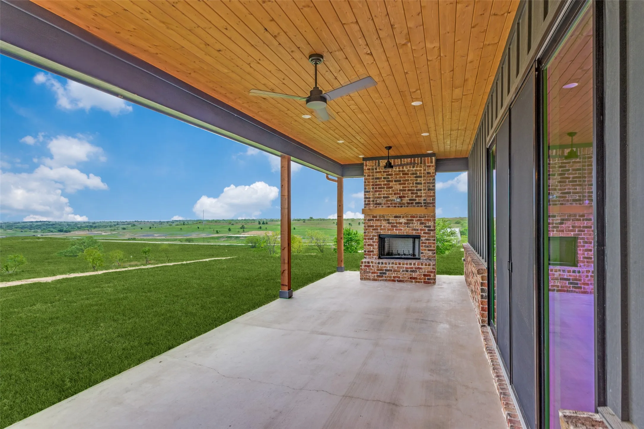 Covered patio featuring a wood-panel ceiling, brick fireplace, and concrete flooring