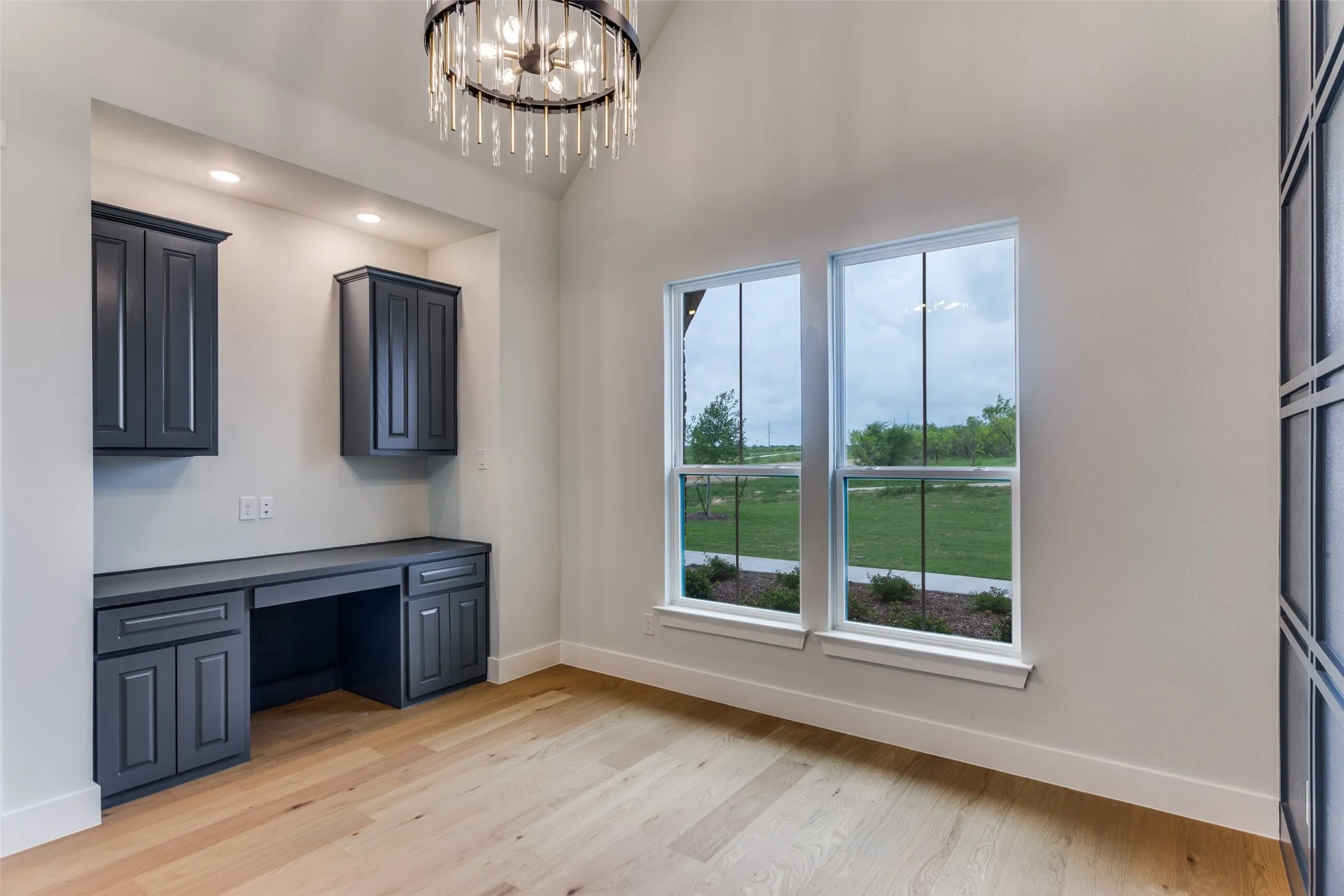 Built-in desk with dark cabinetry, wood-finish flooring, vaulted ceiling, and dual windows