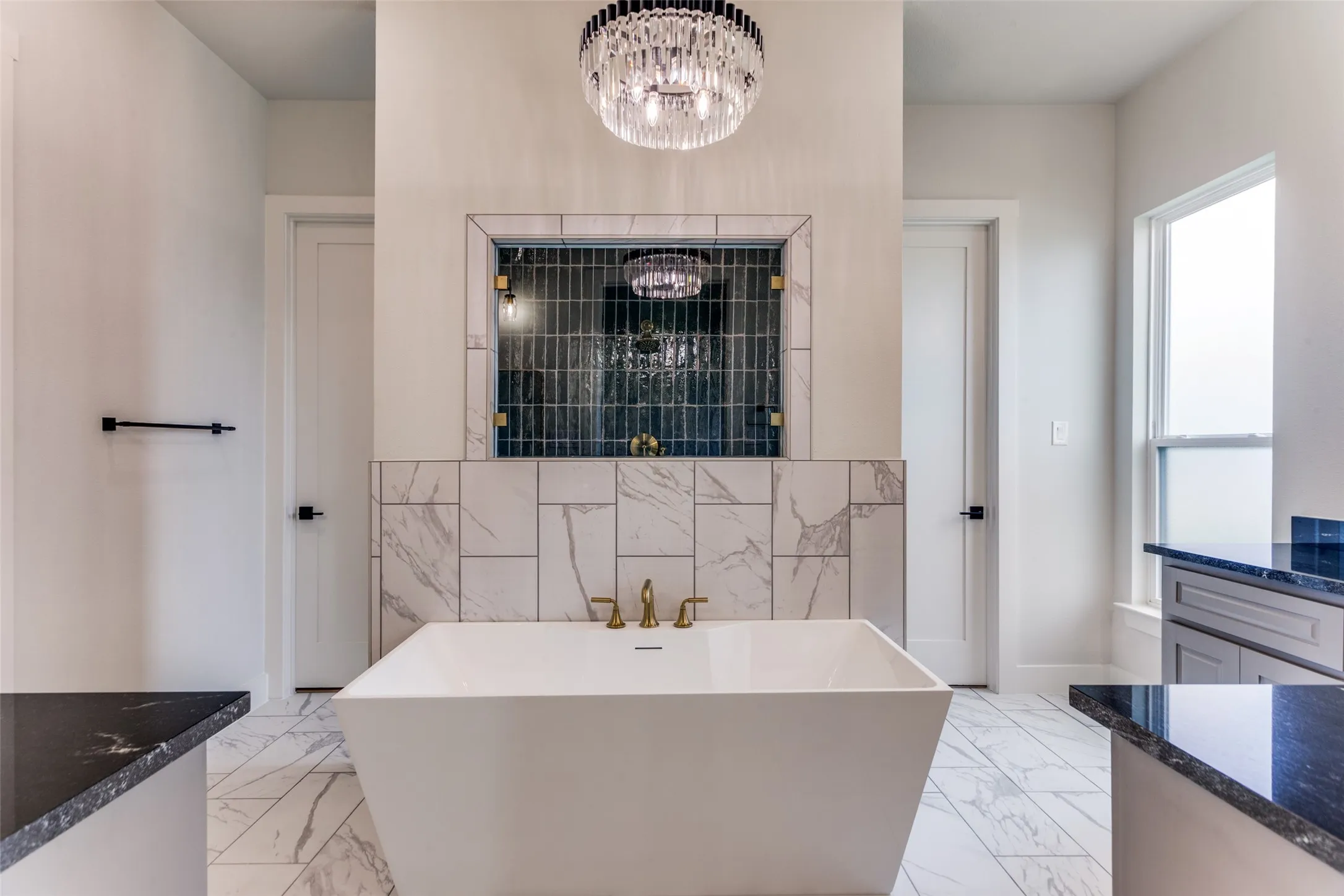Spa-inspired primary bathroom featuring a freestanding soaking tub, marble-finish flooring, and a dual-vanity layout with brass fixtures