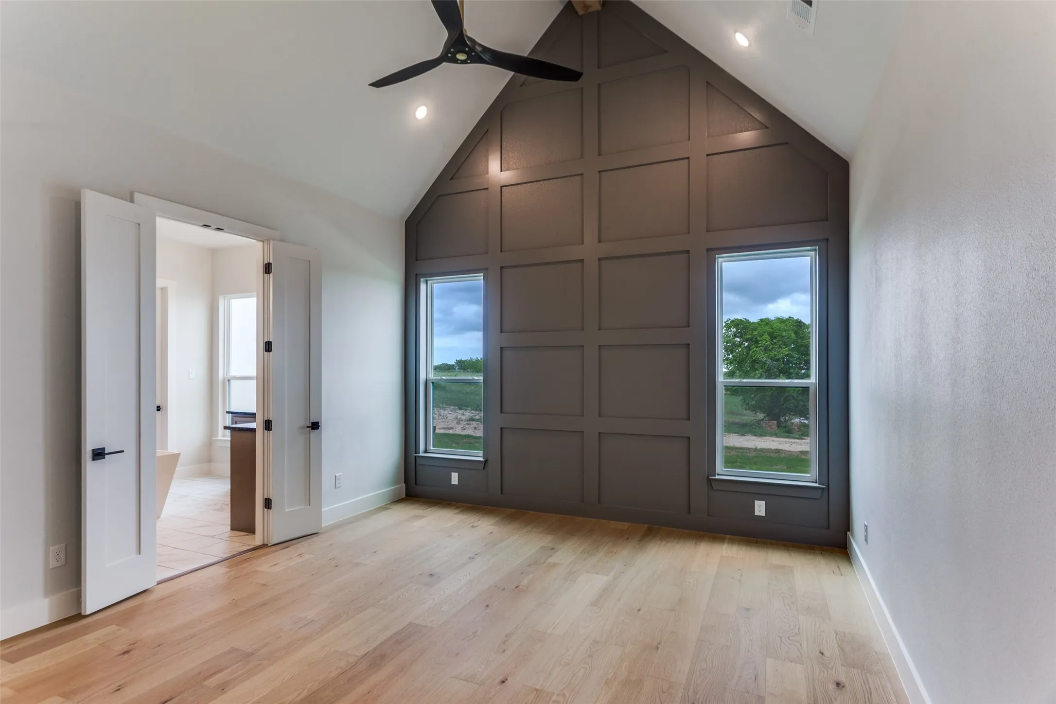 Vaulted ceiling, decorative wall paneling, light wood-finish flooring, recessed lighting, and a modern ceiling fan