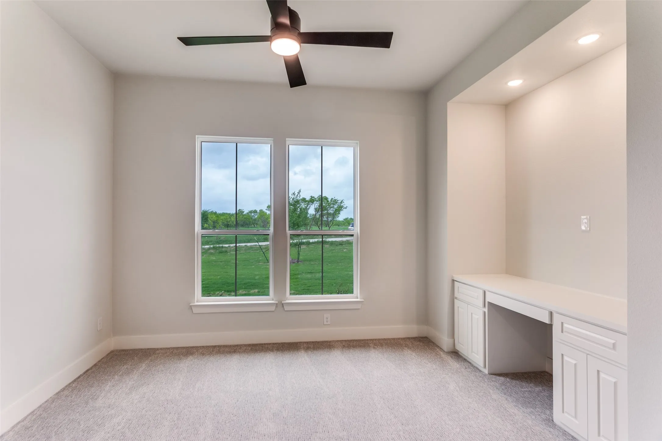 Recessed lighting illuminates a built-in desk with paneled cabinetry, complemented by a ceiling fan