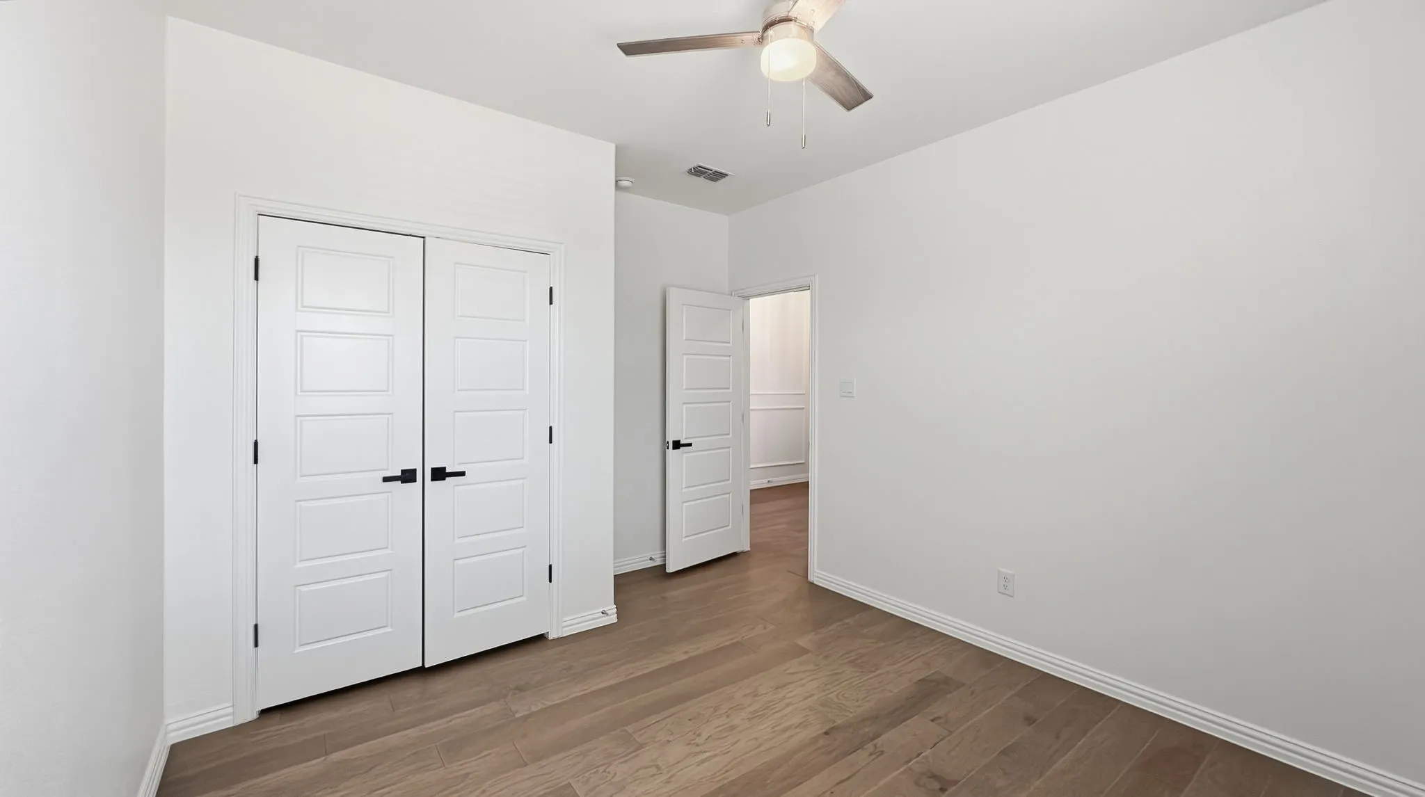 Wood-finish flooring, white paneled doors with matte black hardware, recessed lighting, and a ceiling fan