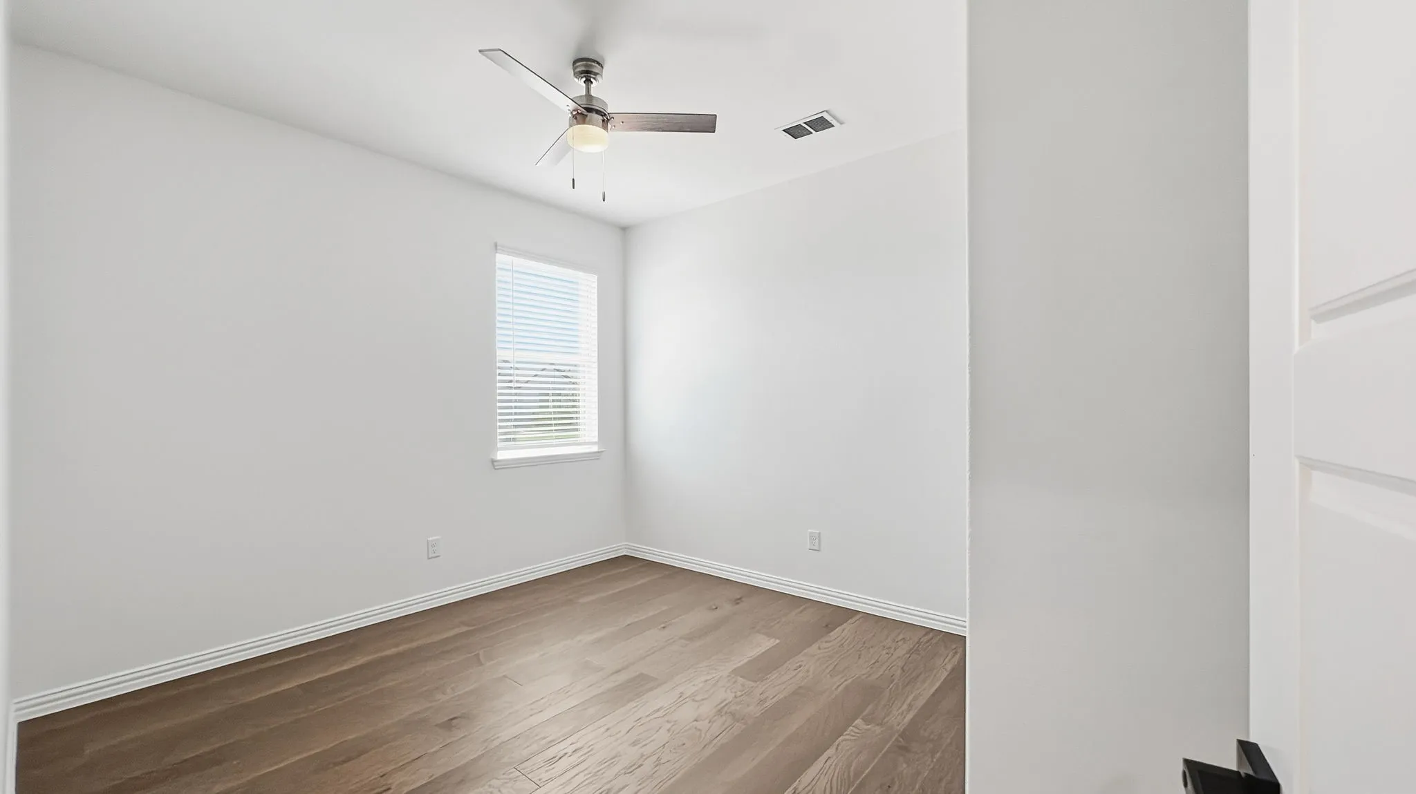 Wood-finish flooring, neutral wall tones, ceiling fan with integrated lighting, window with blinds, and a paneled door