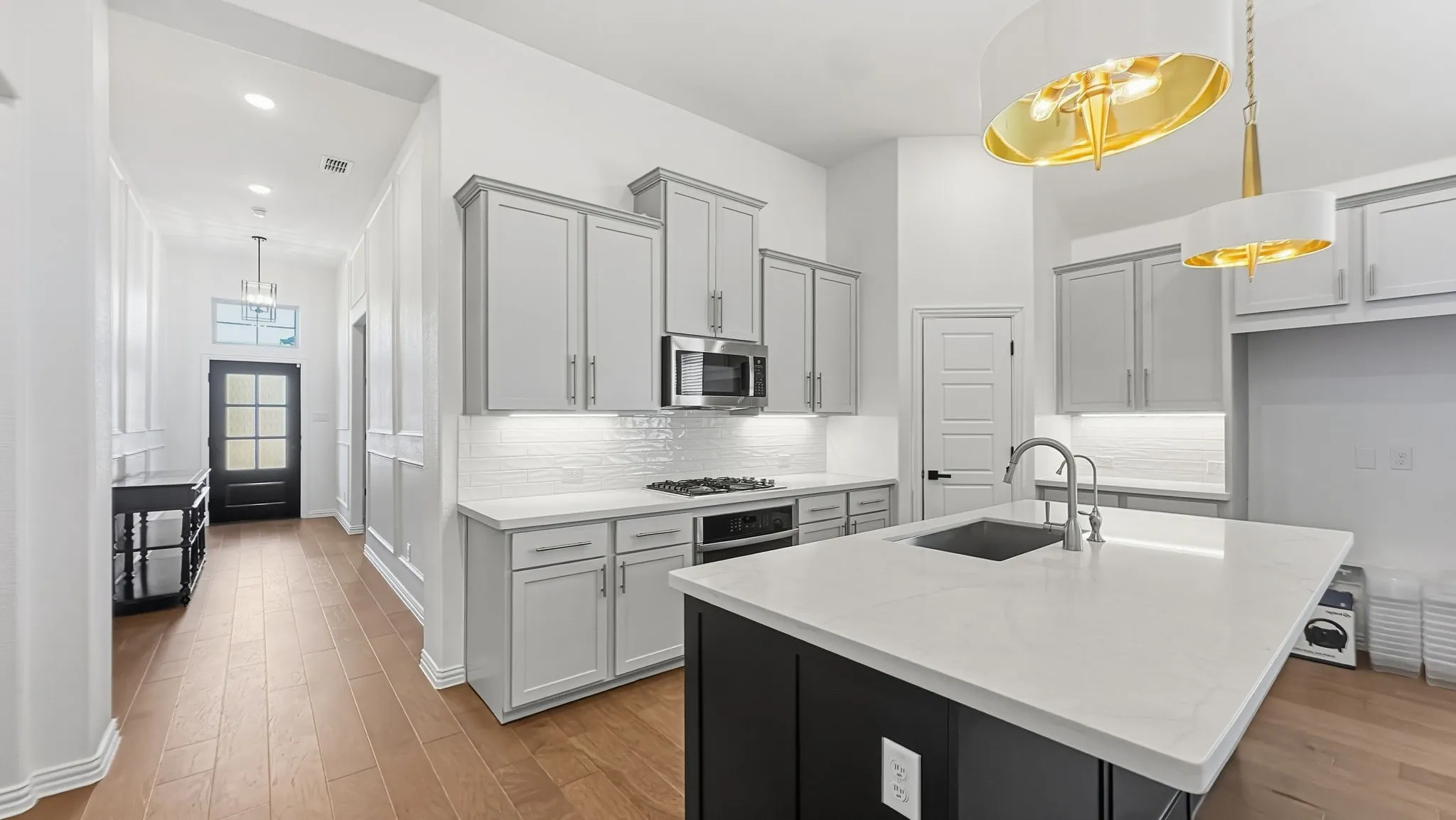 Kitchen featuring light gray cabinetry, stainless steel microwave, white subway tile backsplash, and a large island with an undermount sink