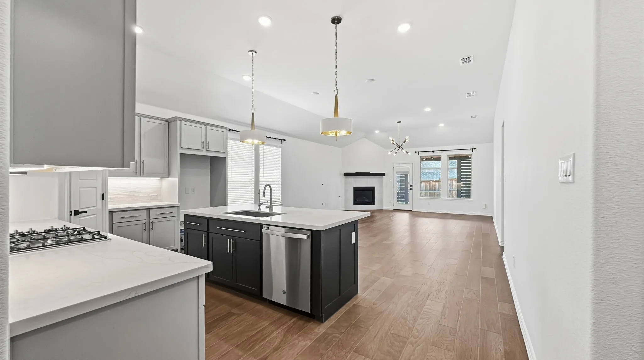 Kitchen featuring a gas cooktop, center island with sink and integrated dishwasher, light wood-finish flooring, and a vaulted ceiling