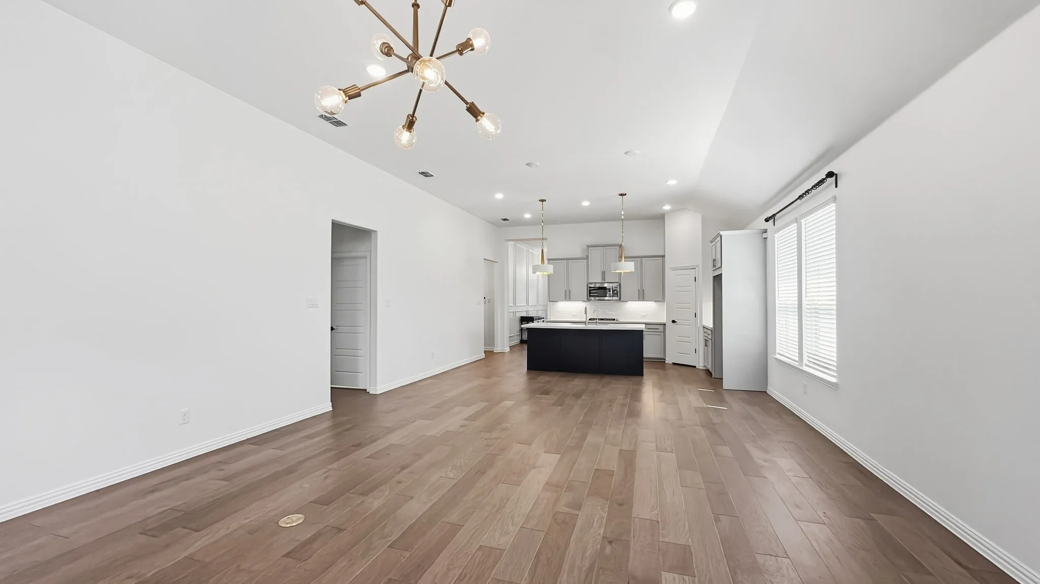 Wood-finish flooring, recessed lighting, and a modern chandelier illuminate this open-concept space