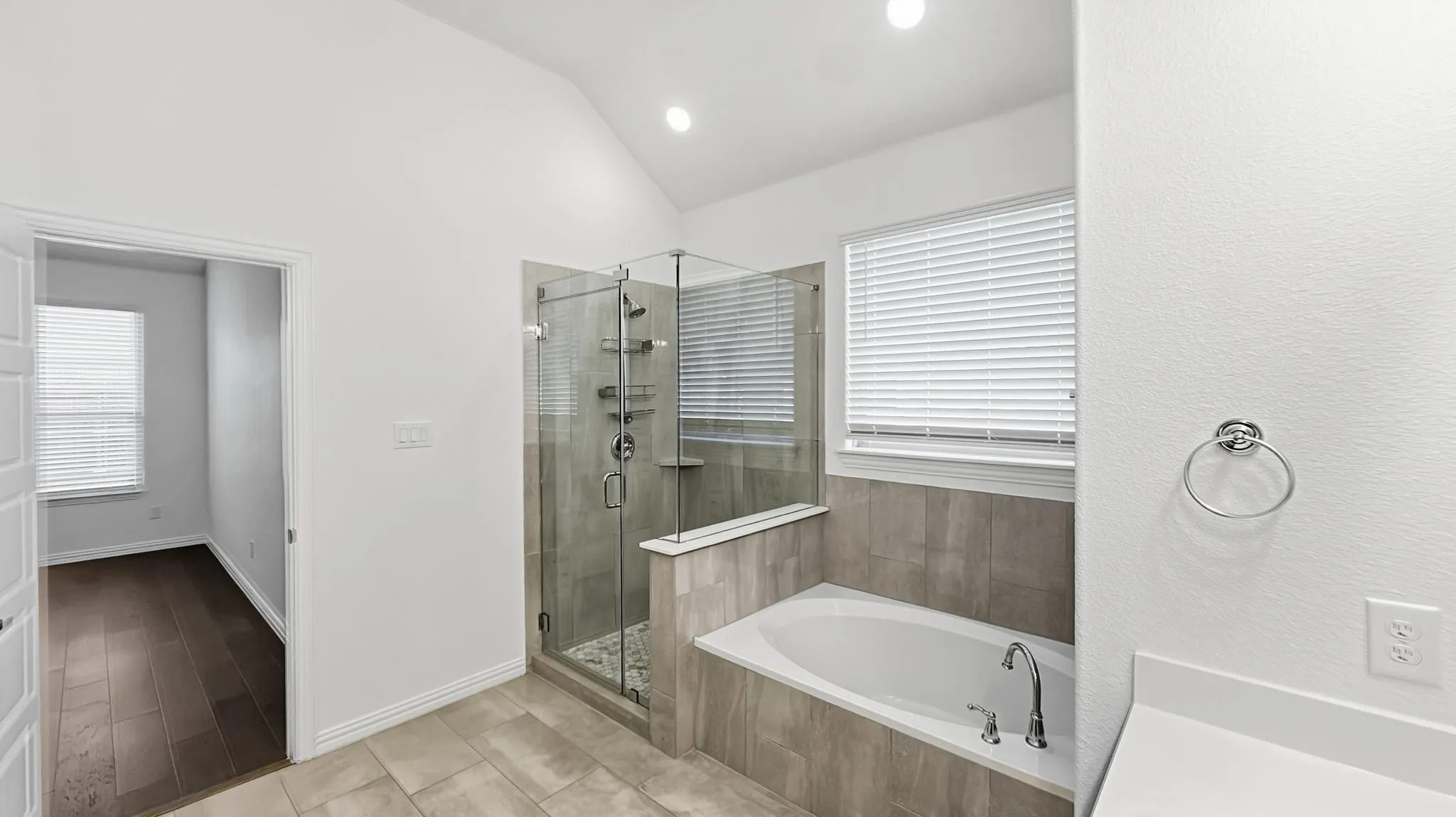 Spacious bathroom featuring a glass-enclosed shower, built-in soaking tub, and vaulted ceiling