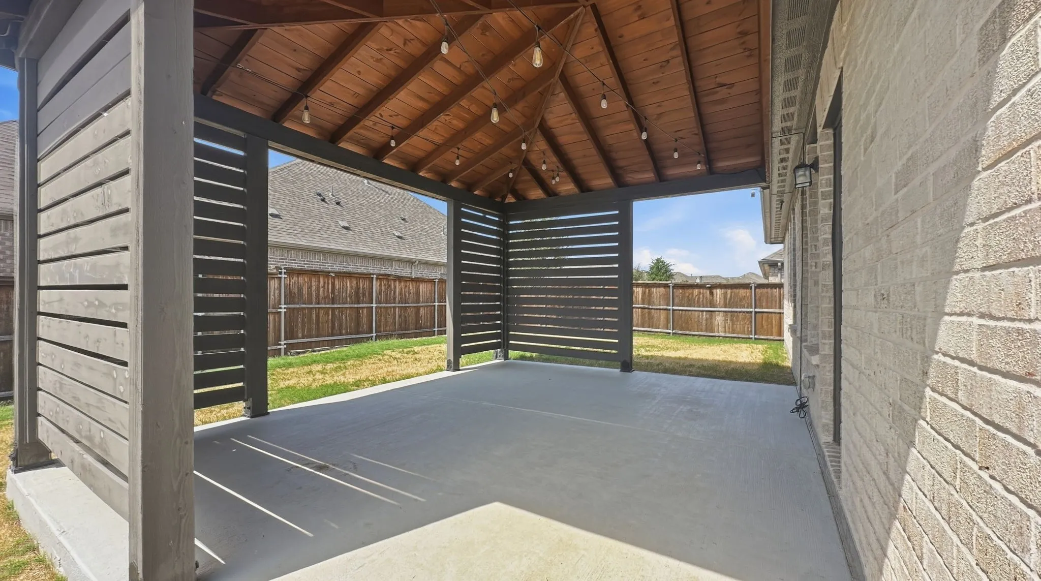 Covered patio featuring a wood-finish ceiling, concrete flooring, and slatted privacy screens