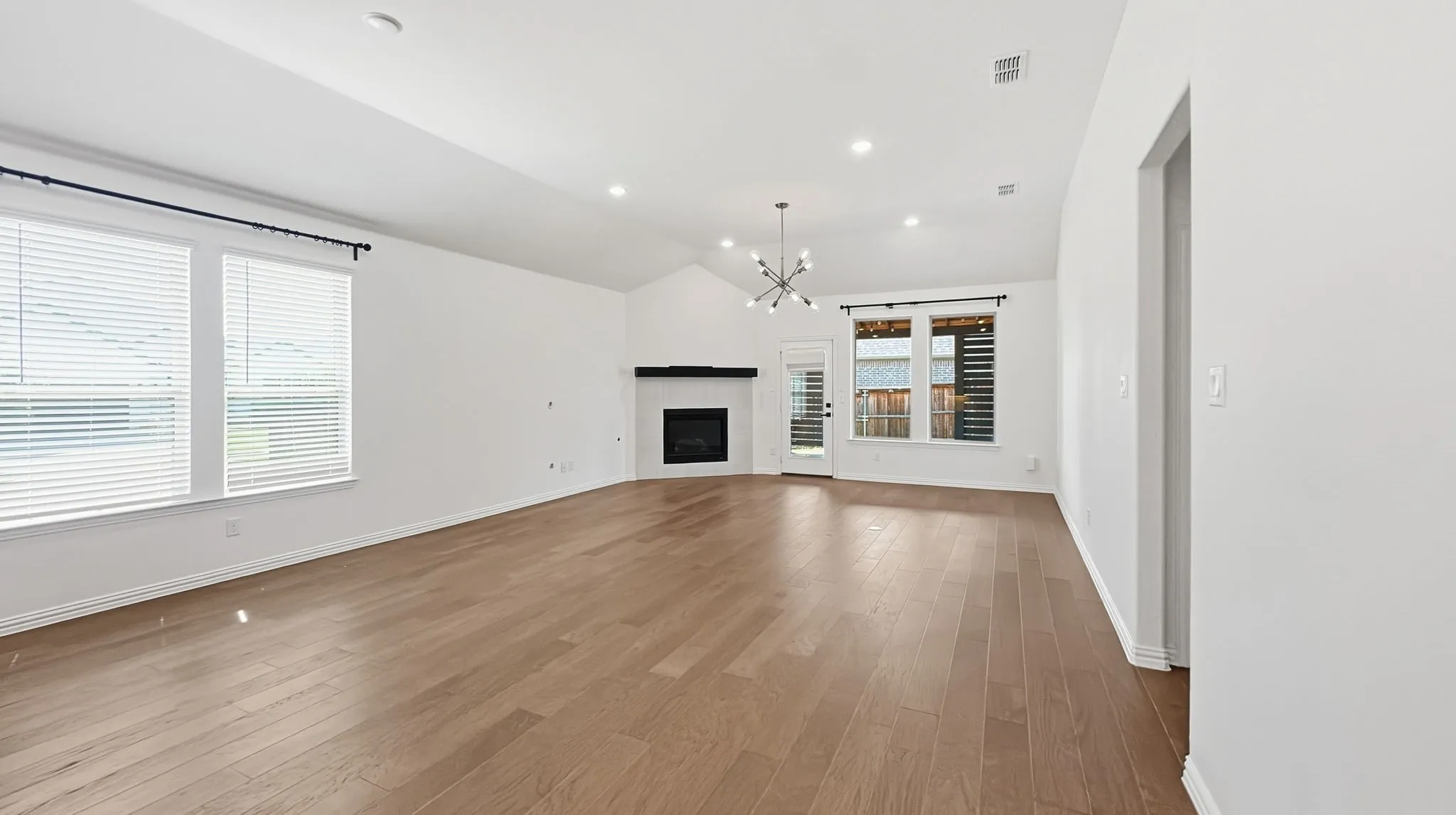 Vaulted ceiling, recessed lighting, wood-finish flooring, fireplace, and a contemporary chandelier