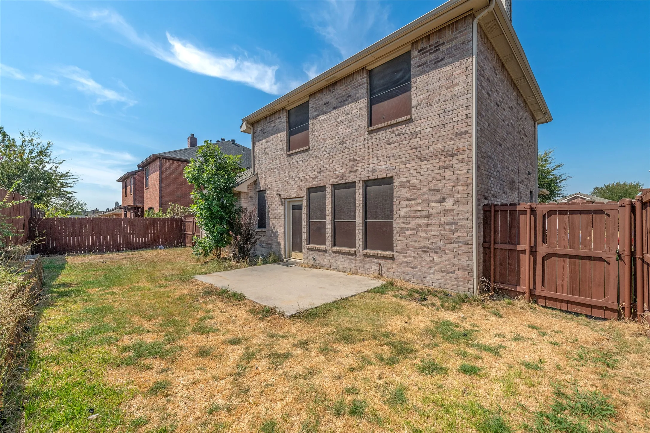 Brick exterior with multiple windows, ground-level patio, and wood fencing enclosing the backyard