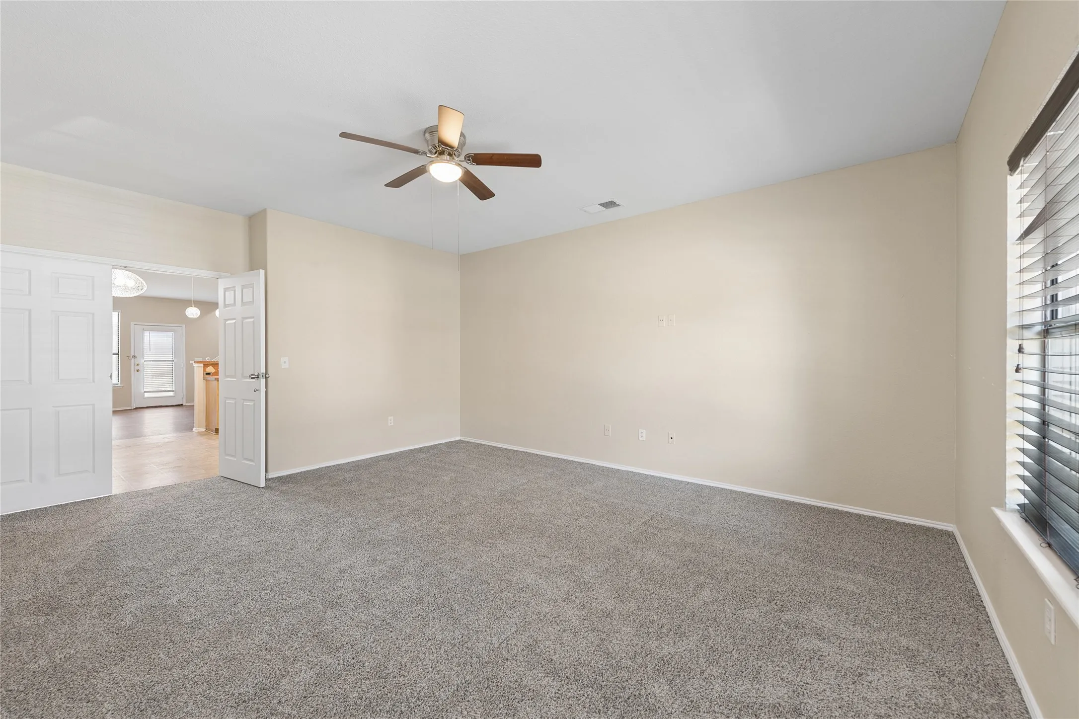 Spacious room featuring neutral carpet, a ceiling fan with light fixture, and window blinds