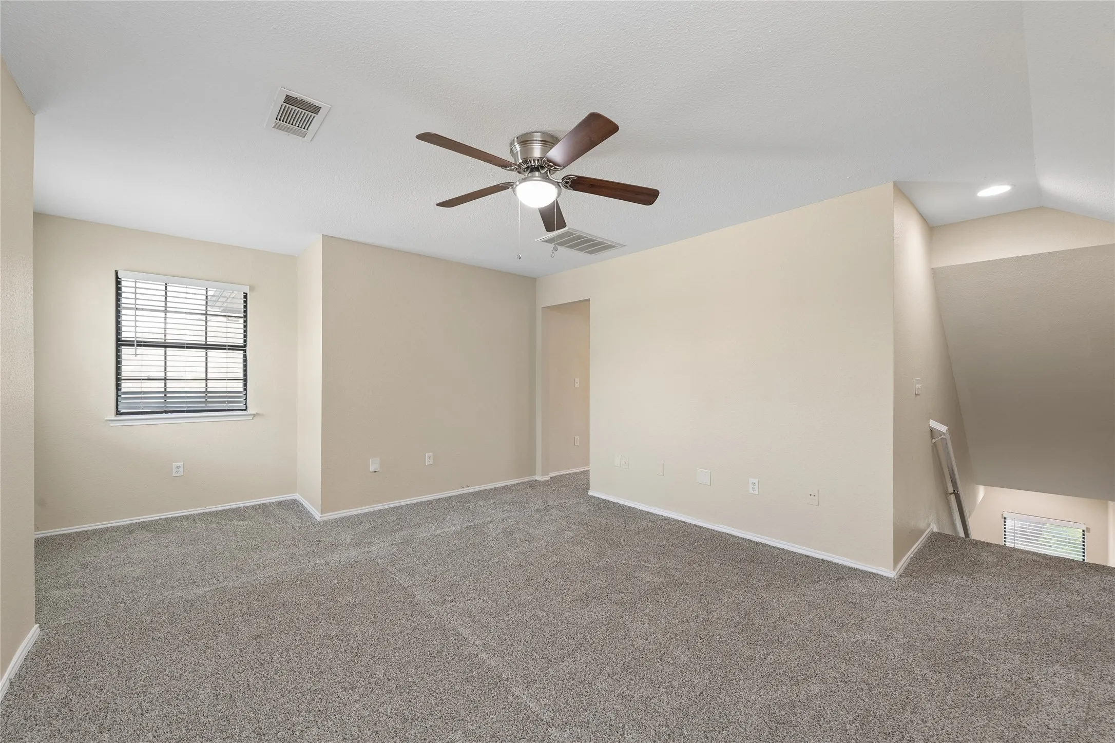 Expansive carpeted area with a ceiling fan, window with blinds, and neutral wall tones