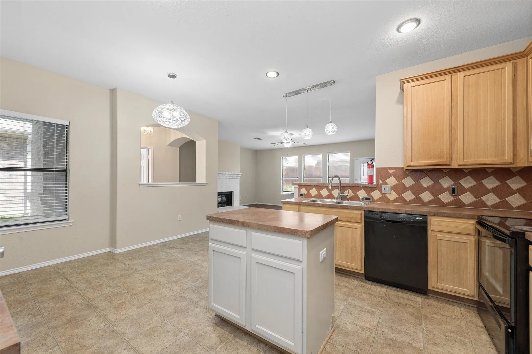 Kitchen featuring a central island, light wood cabinetry, tile backsplash, and a double basin sink