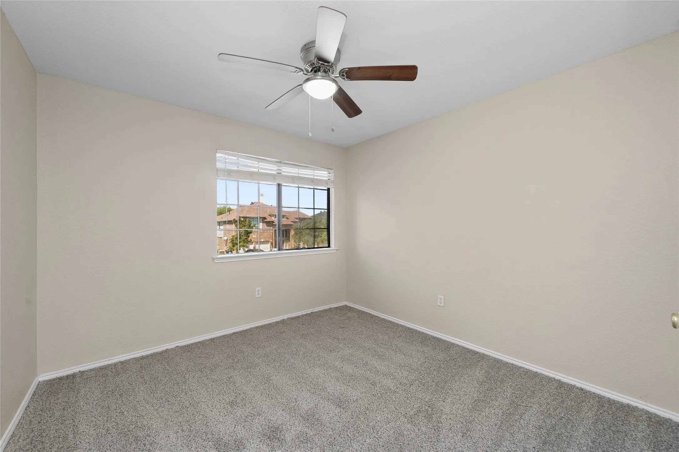 Neutral-toned walls, ceiling fan with light fixture, large window with blinds, and gray carpeted flooring