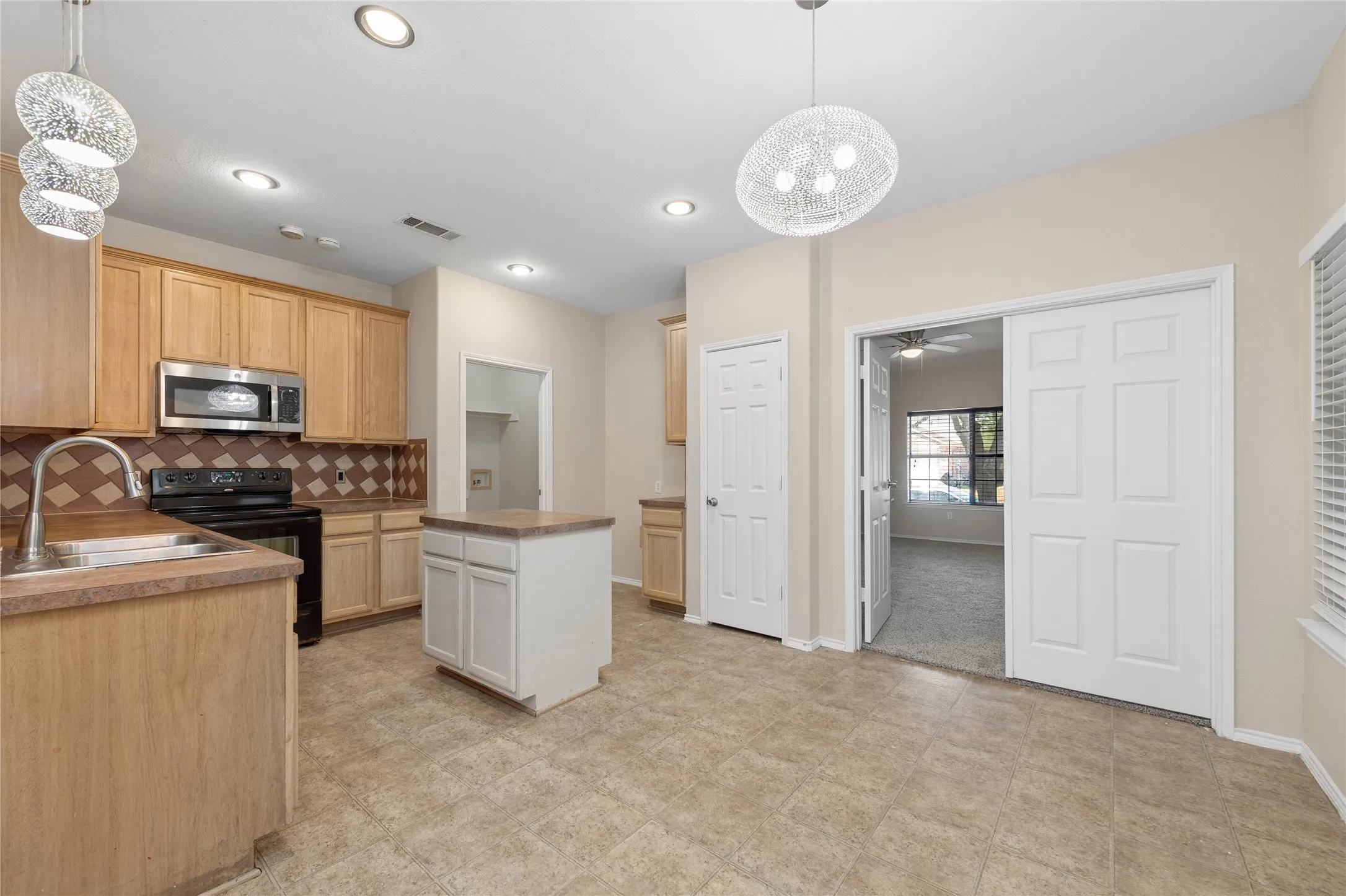Kitchen featuring light wood-finish cabinetry, stainless steel microwave, black electric range, and a central island