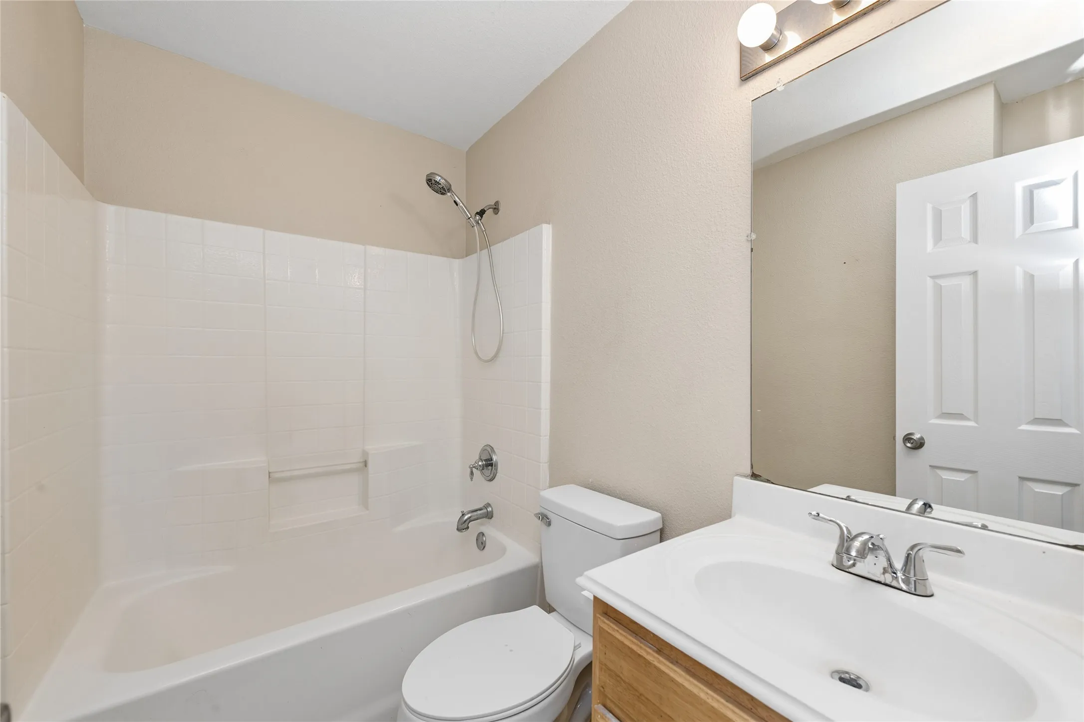 Wood-finish vanity with an integrated sink and chrome faucet, large wall mirror, and a full bathtub with a shower and white surround