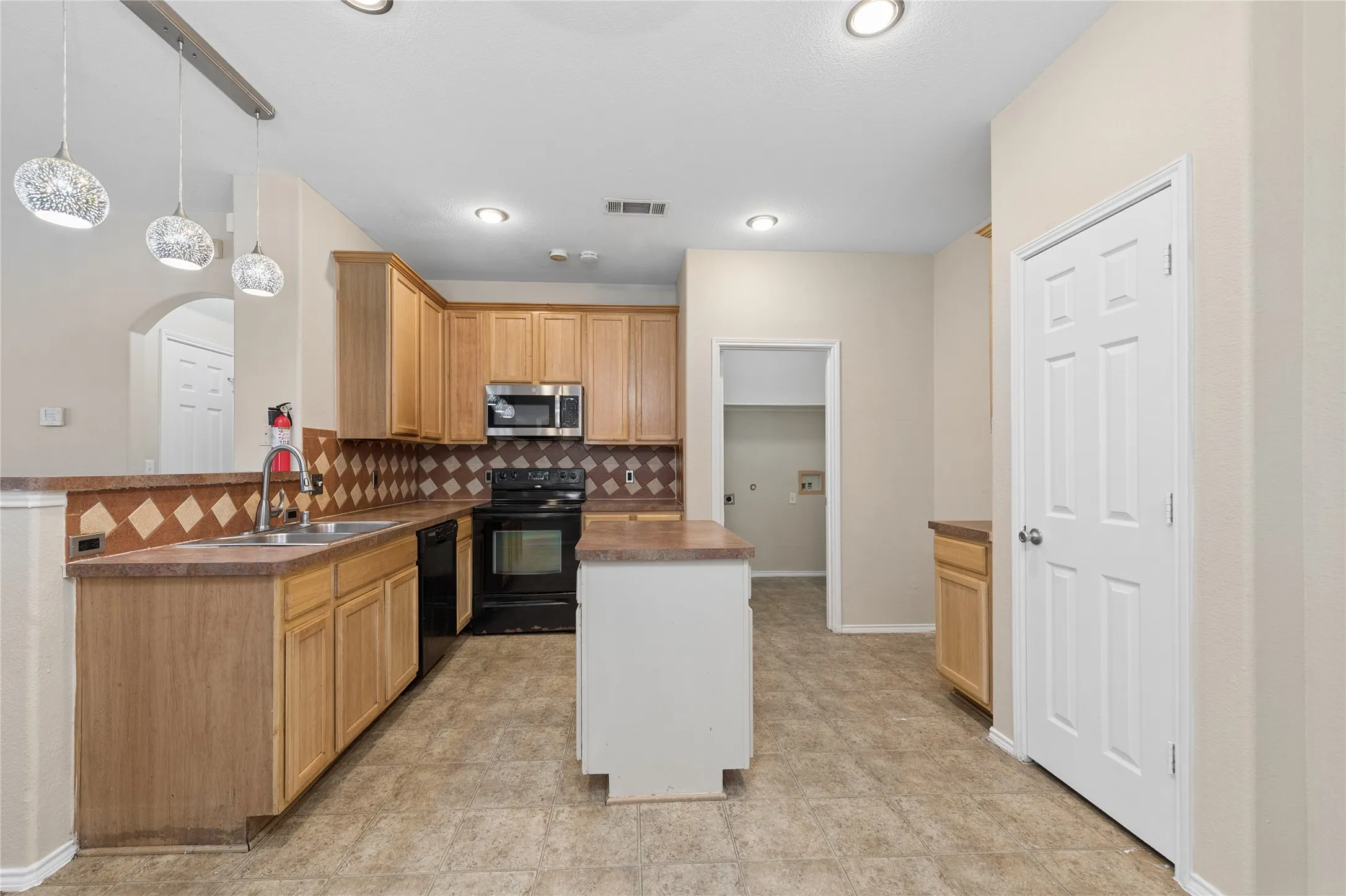 Kitchen featuring wood cabinetry, stainless steel microwave, black appliances, and a central island