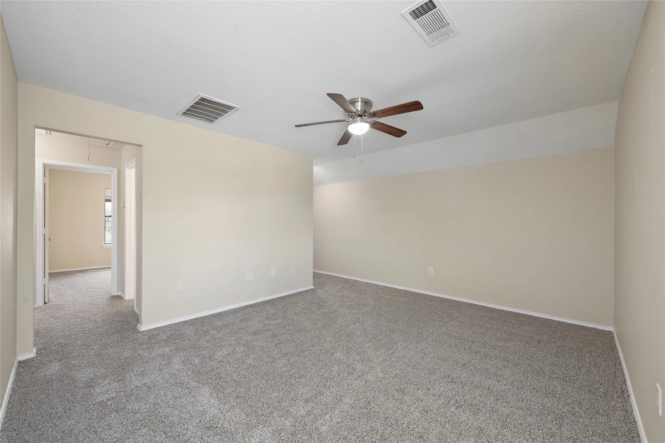 Neutral-toned walls, textured gray carpeting, ceiling fan with integrated lighting, and recessed ceiling vents