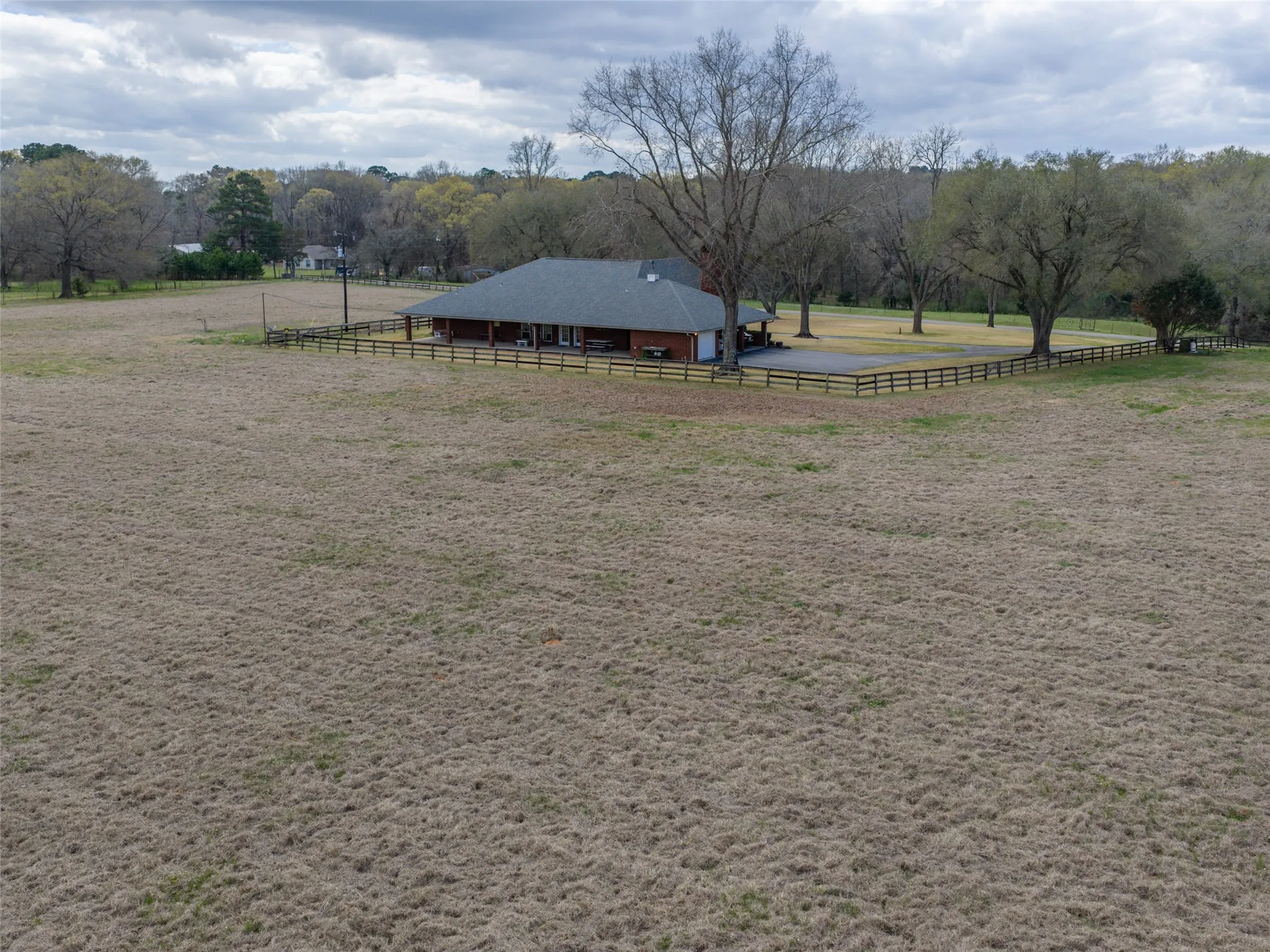 Expansive field surrounding a residence with a dark-pitched roof, brick exterior, and a covered porch