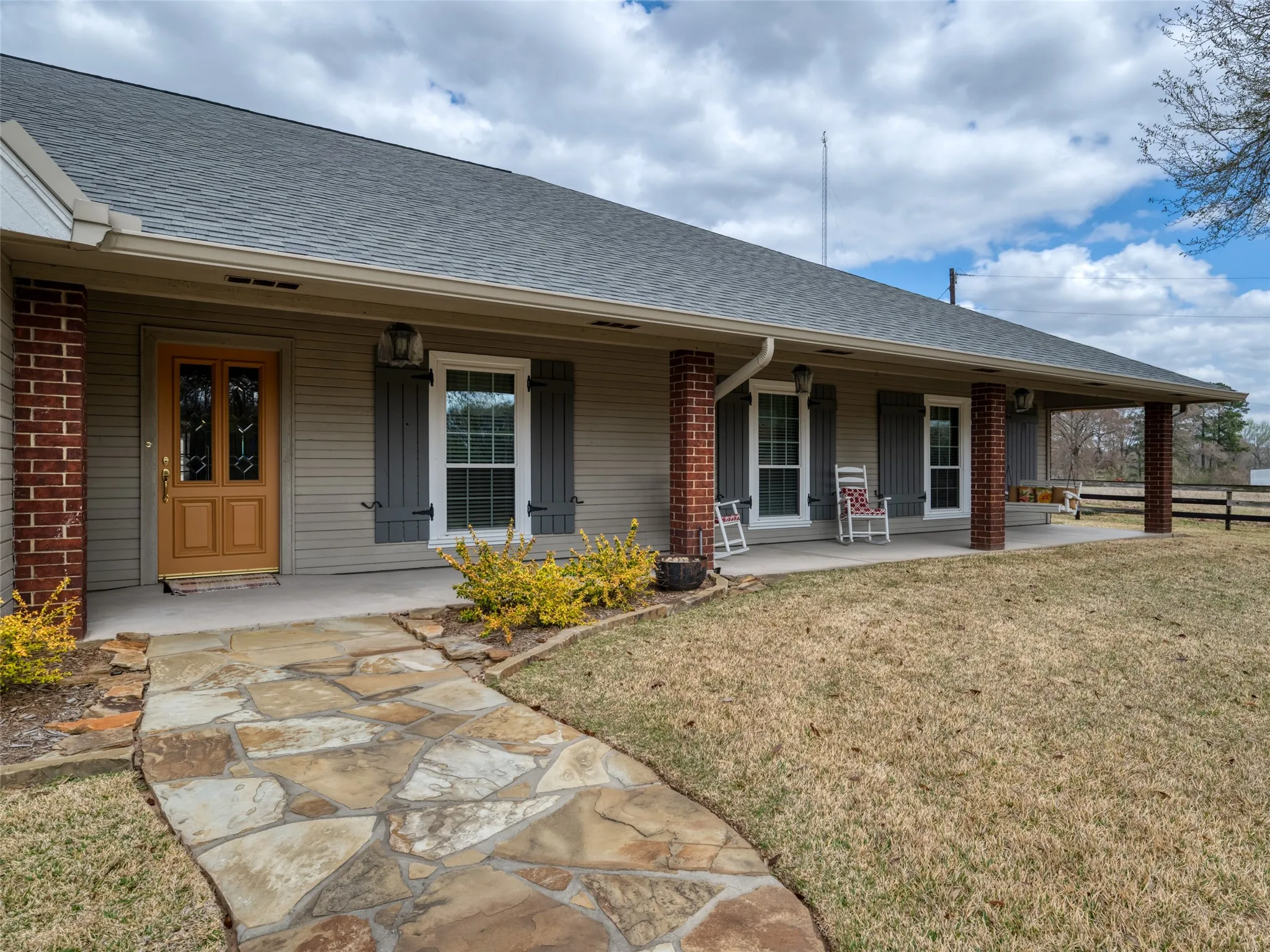 Expansive covered front porch with brick columns, a decorative wood entry door, and stone pathway