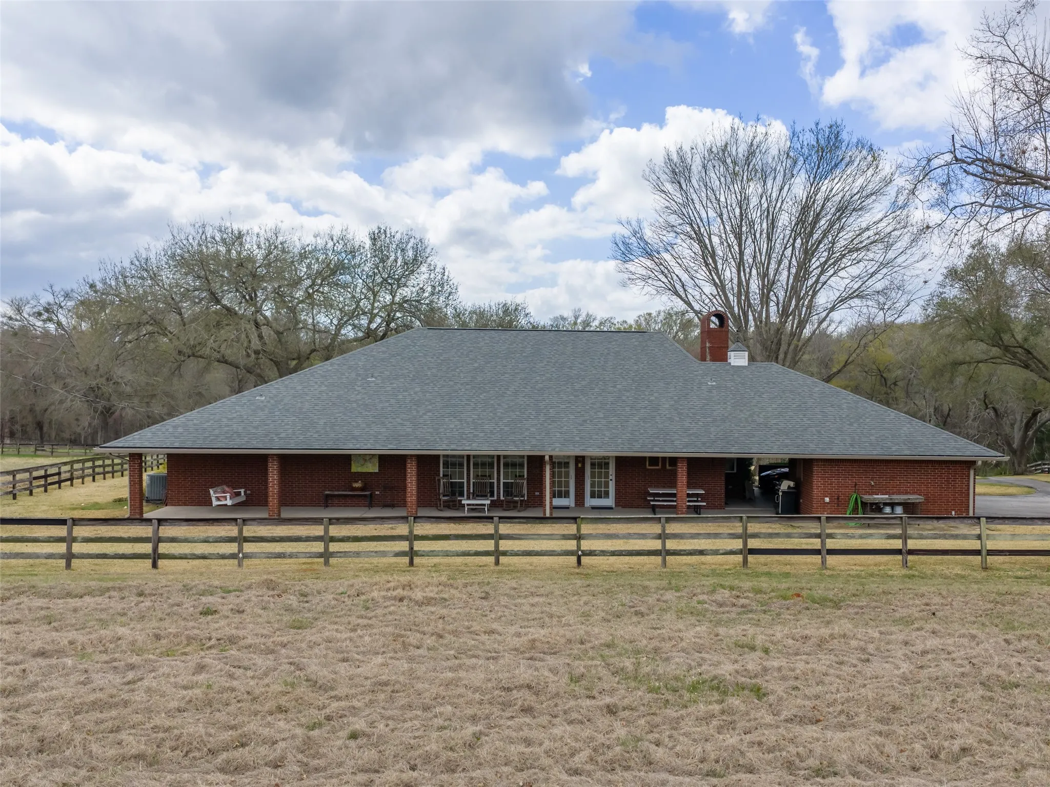 Brick exterior with a covered porch extending across the rear, featuring multiple entry points and a wood fence