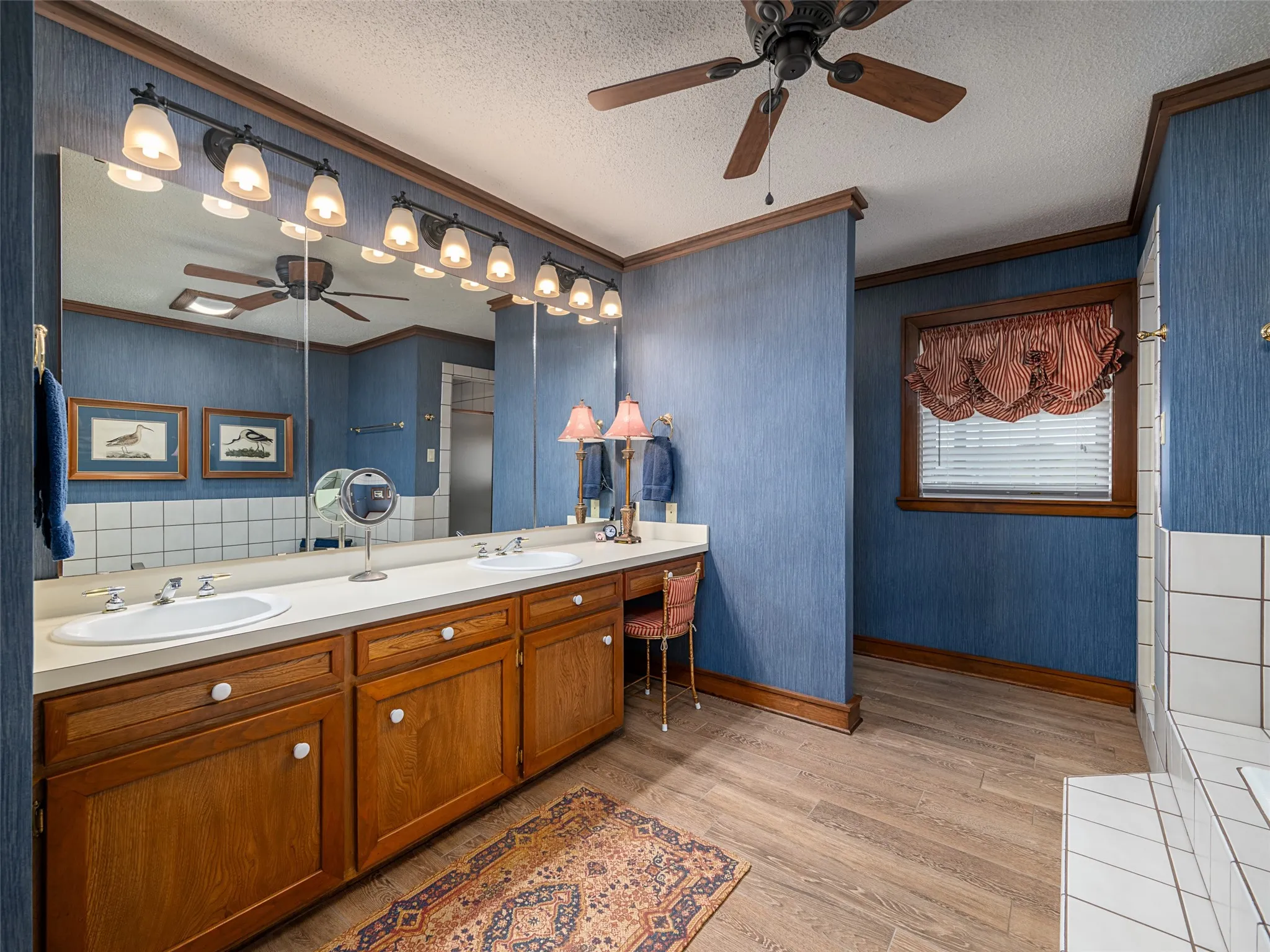 Double vanity with integrated sinks, extensive counter space, wood-finish flooring, wood cabinetry with white knob hardware, and overhead track lighting