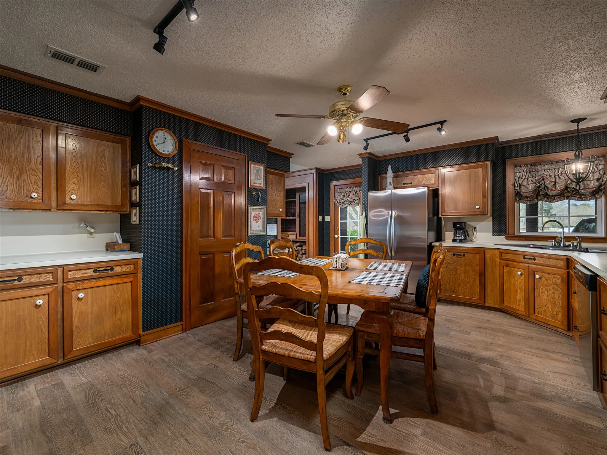 Wood-finish flooring, wood cabinetry with white countertops, stainless steel refrigerator, and recessed lighting
