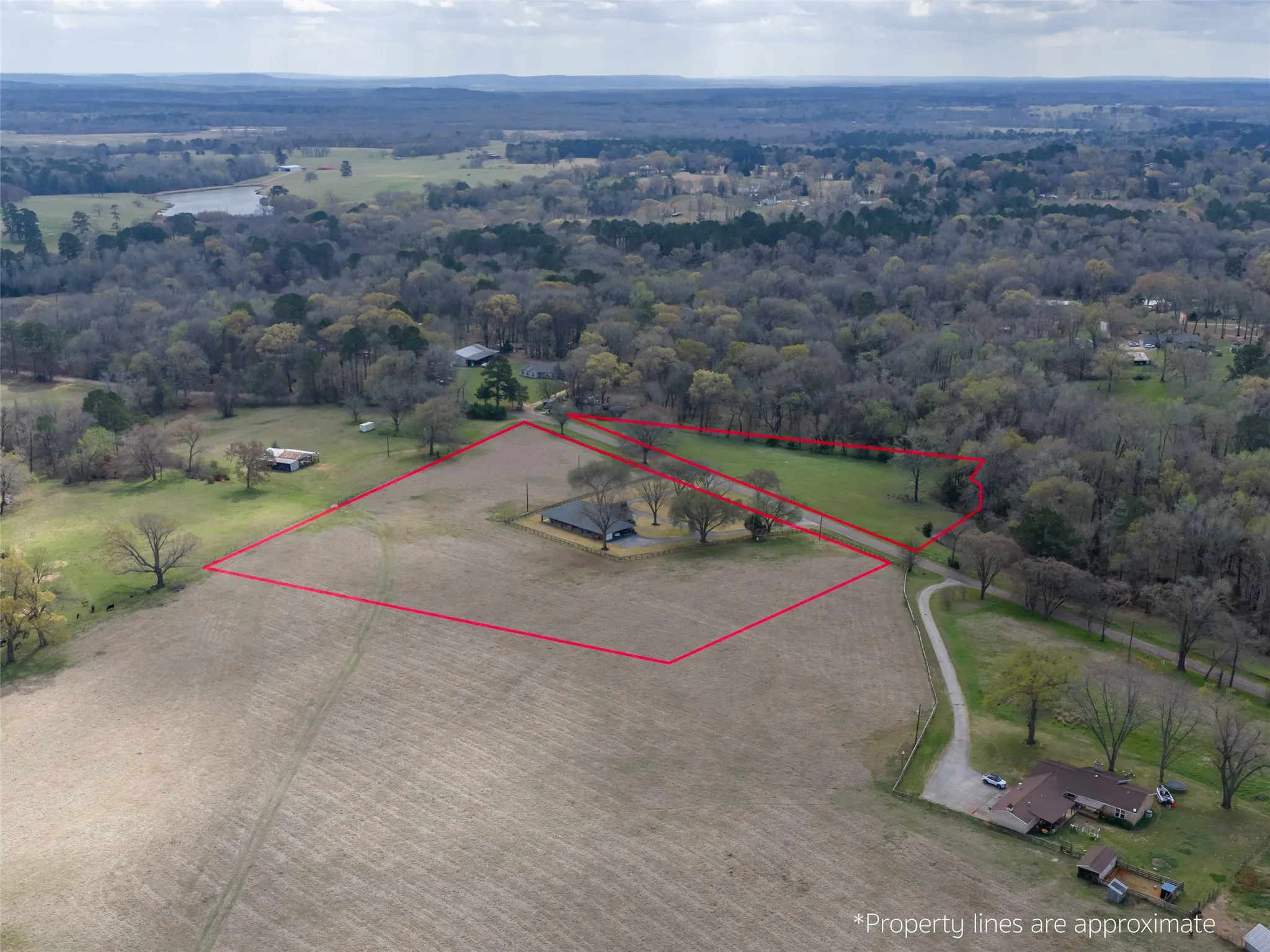 Expansive land parcel featuring open fields, wooded areas, and a visible body of water in the distance